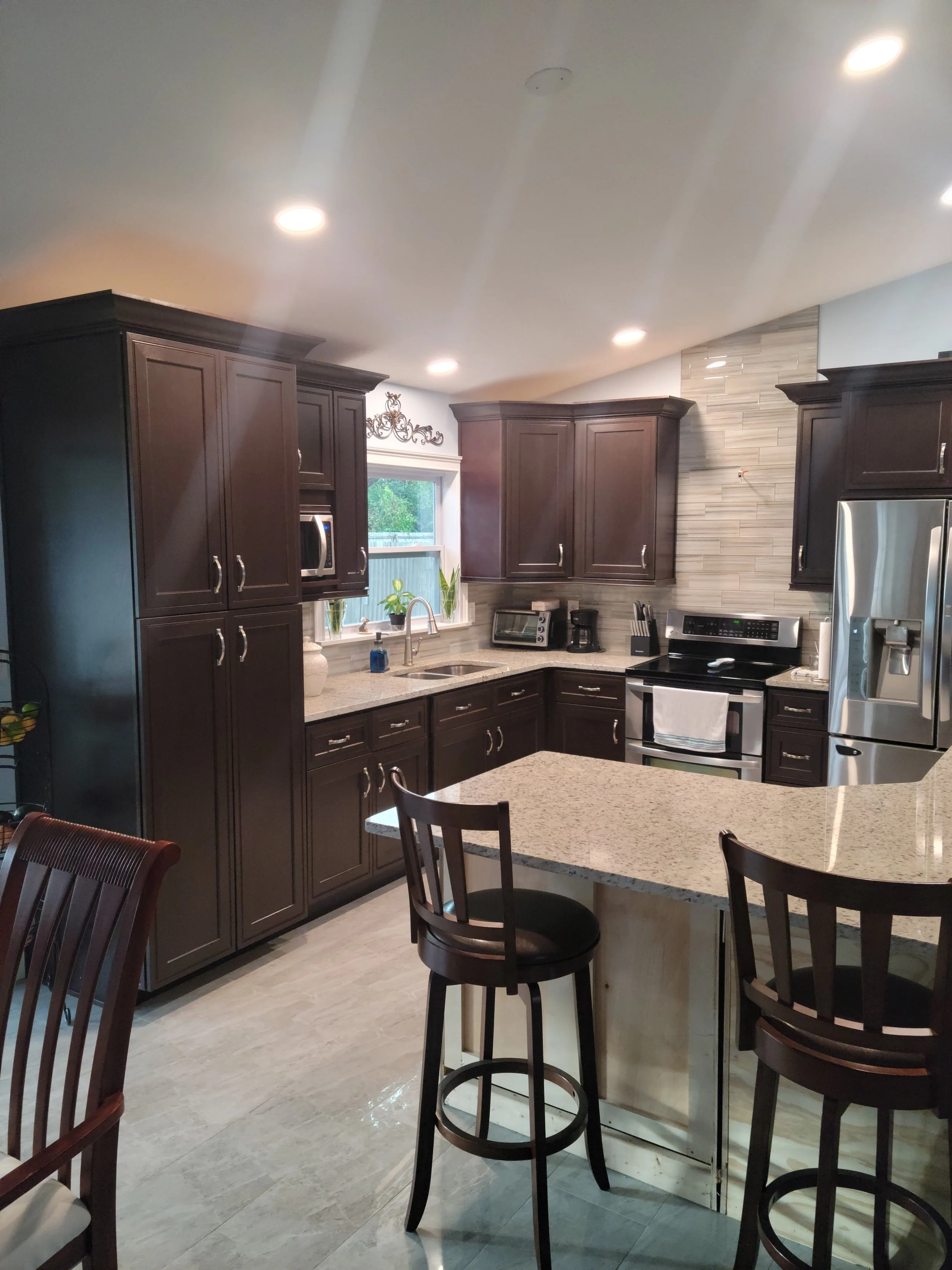 Modern kitchen with dark wood cabinets, granite countertops, stainless steel appliances, and a breakfast island with bar stools.