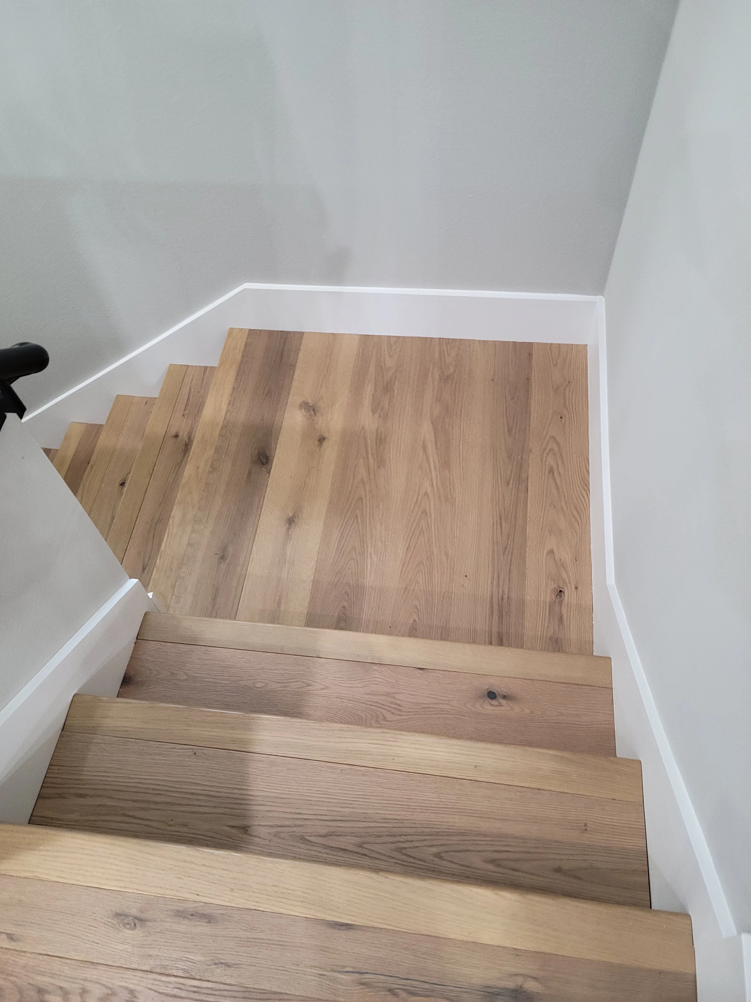 Wooden staircase with light-colored treads and white trim at the corner of a room.
