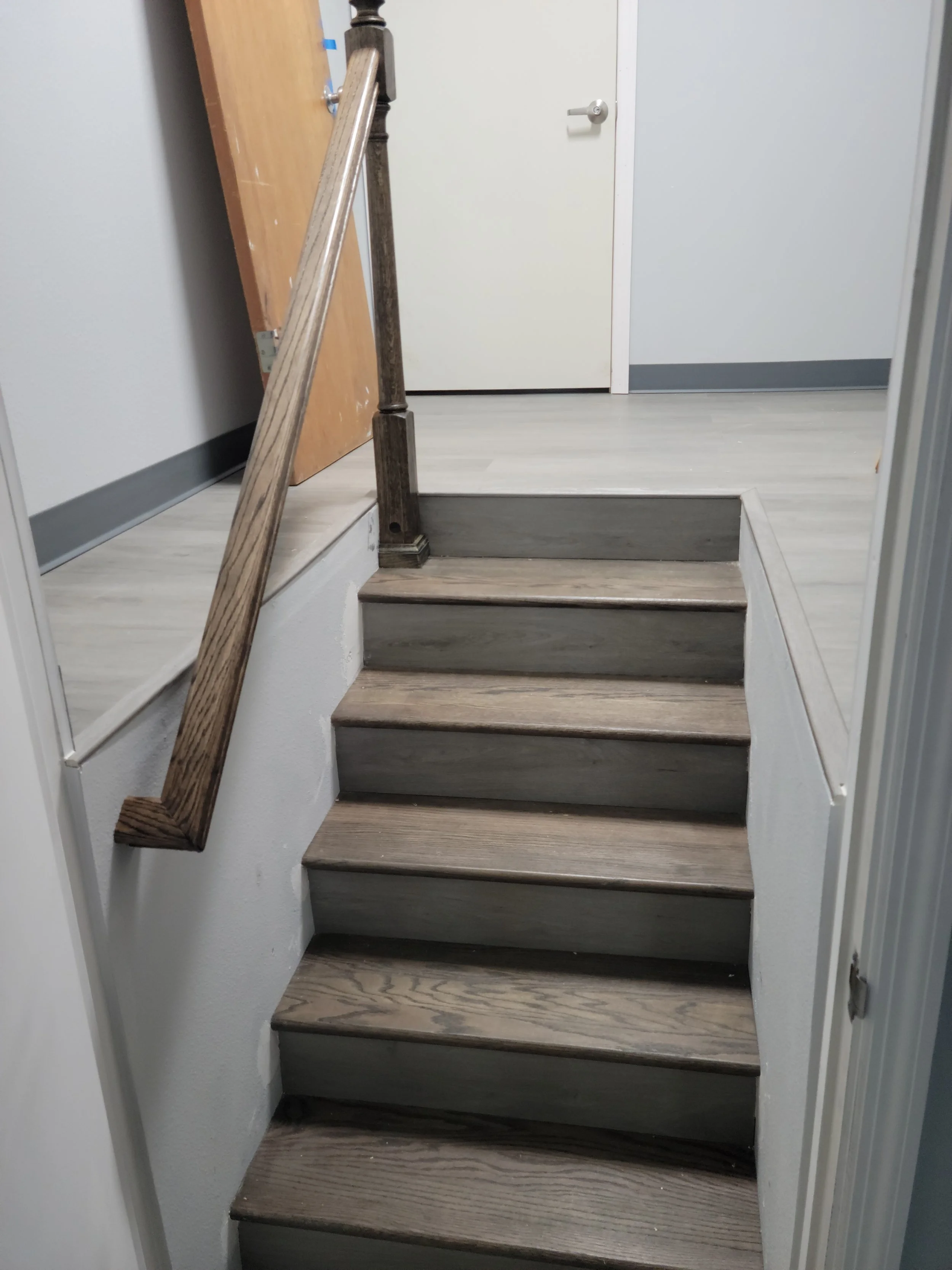 Image of a small set of wooden stairs leading to a door, with a handrail on one side and a temporary barrier or walls on either side.