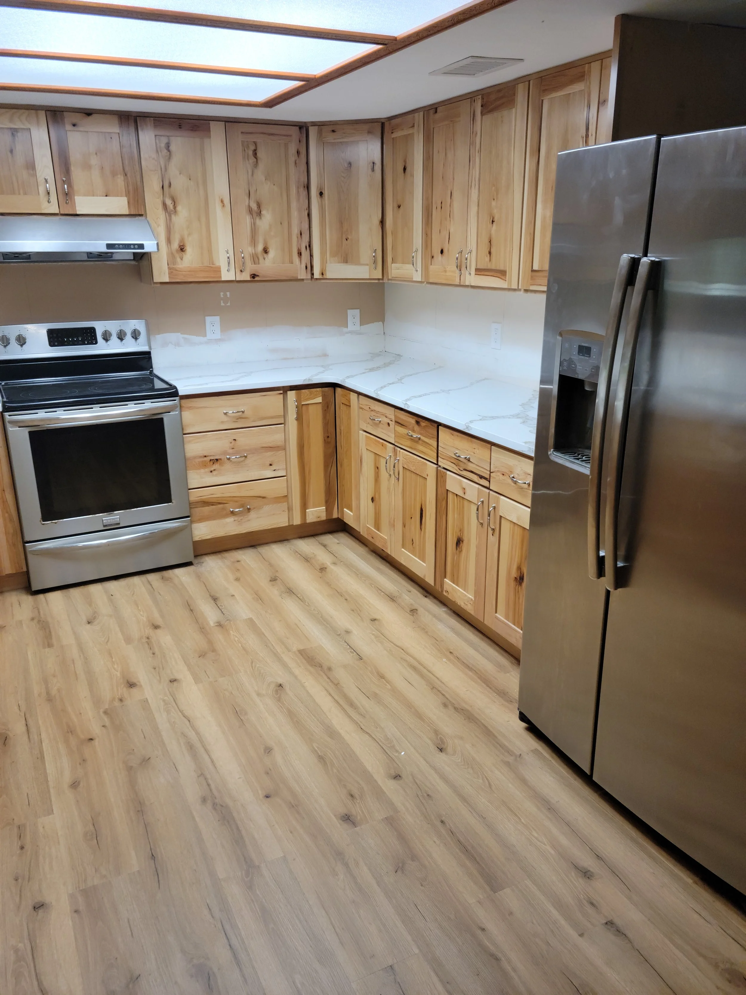 Kitchen with wooden cabinets, marble countertops, stainless steel appliances including a refrigerator and oven, and wood flooring.