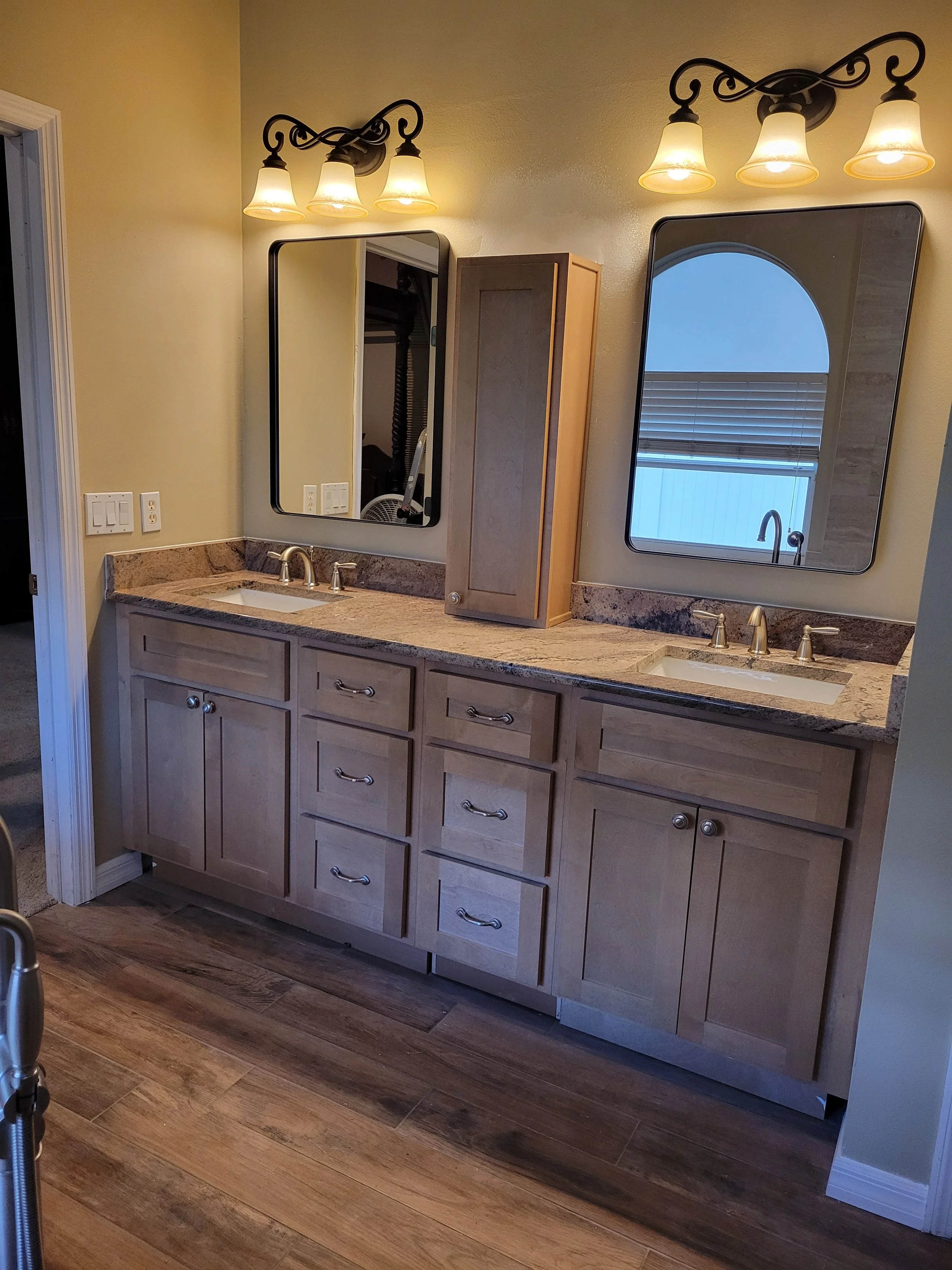 Bathroom vanity with two sinks, light wood cabinets, granite countertops, two mirrors, and wall-mounted light fixtures.