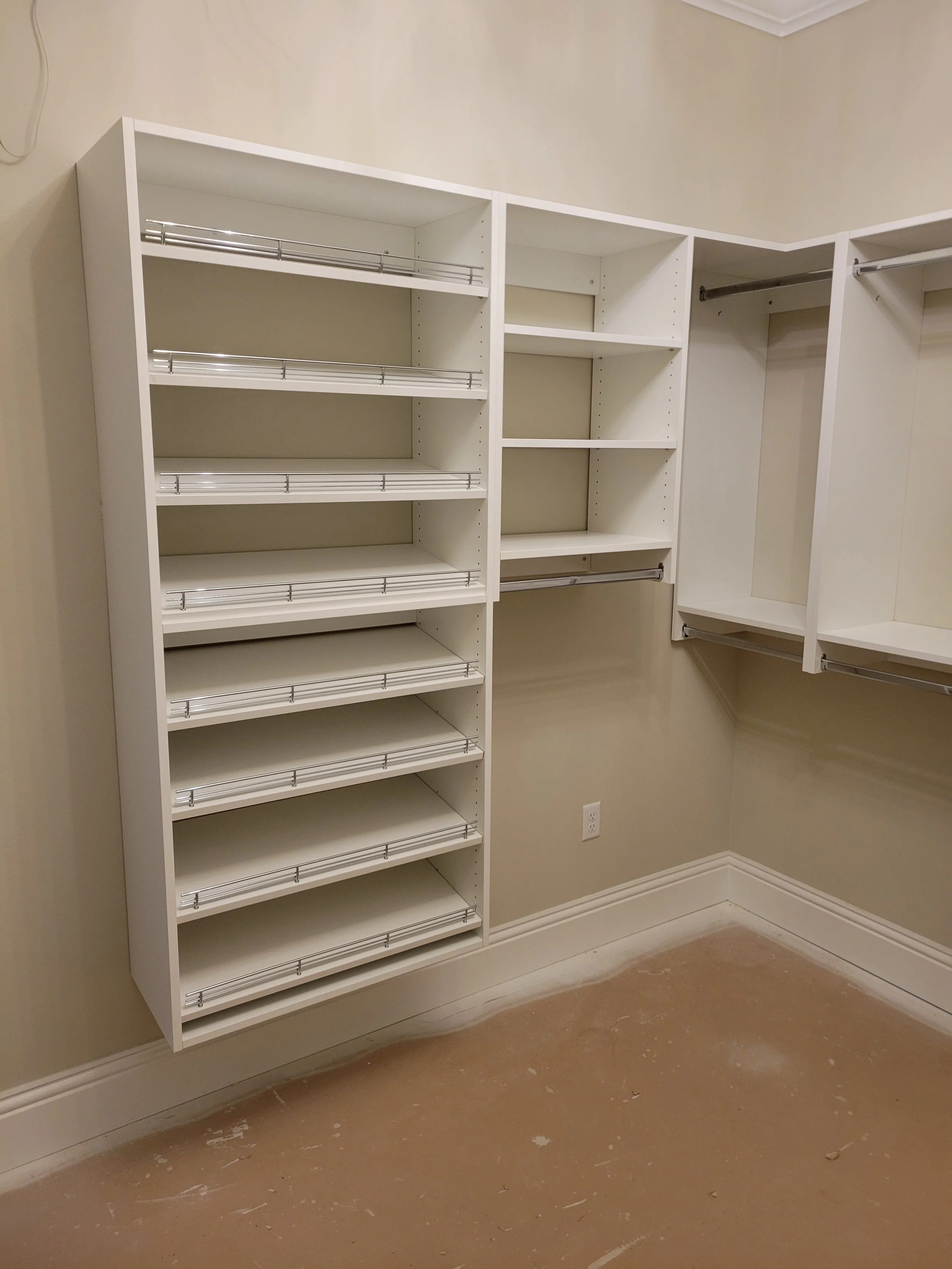 White empty closet shelving and hanging rods against a beige wall, with a light brown floor.