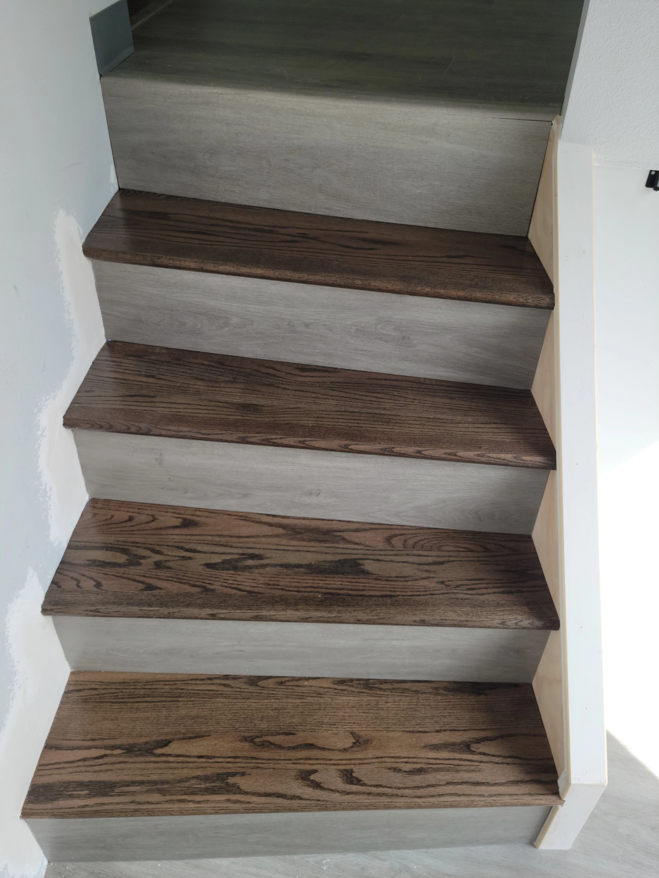 Wooden staircase with alternating dark and light wood treads and white risers.