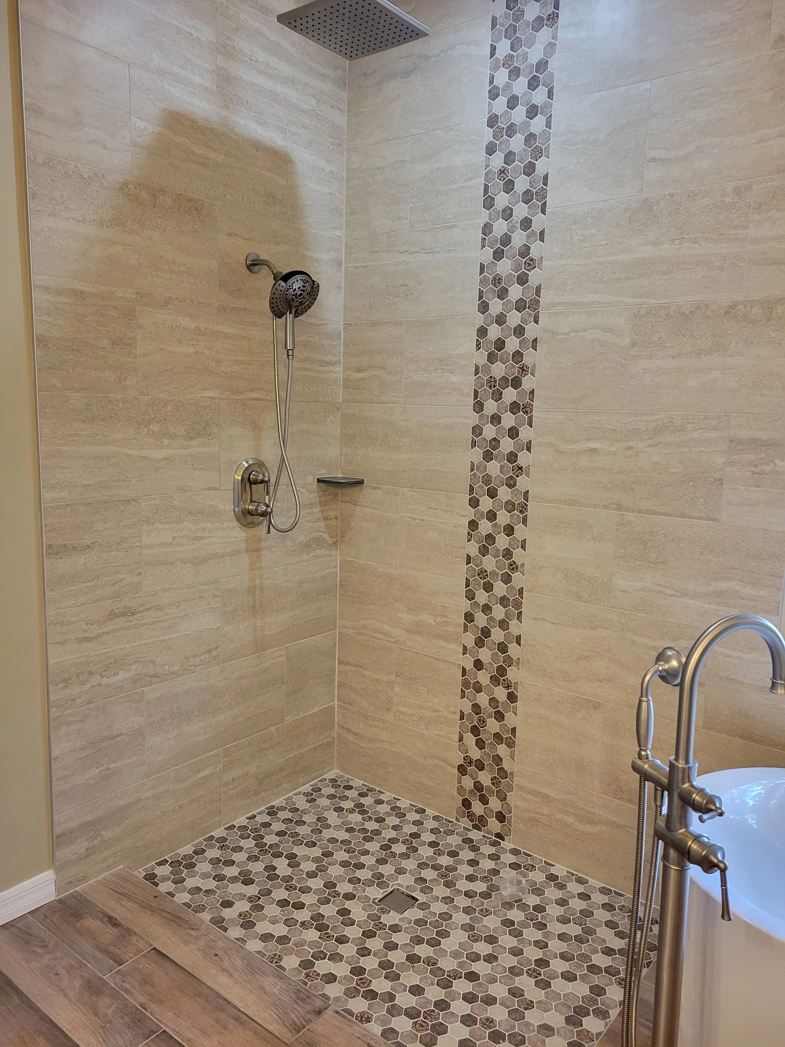 Walk-in shower with beige tile walls featuring a strip of small hexagonal mosaic tiles.