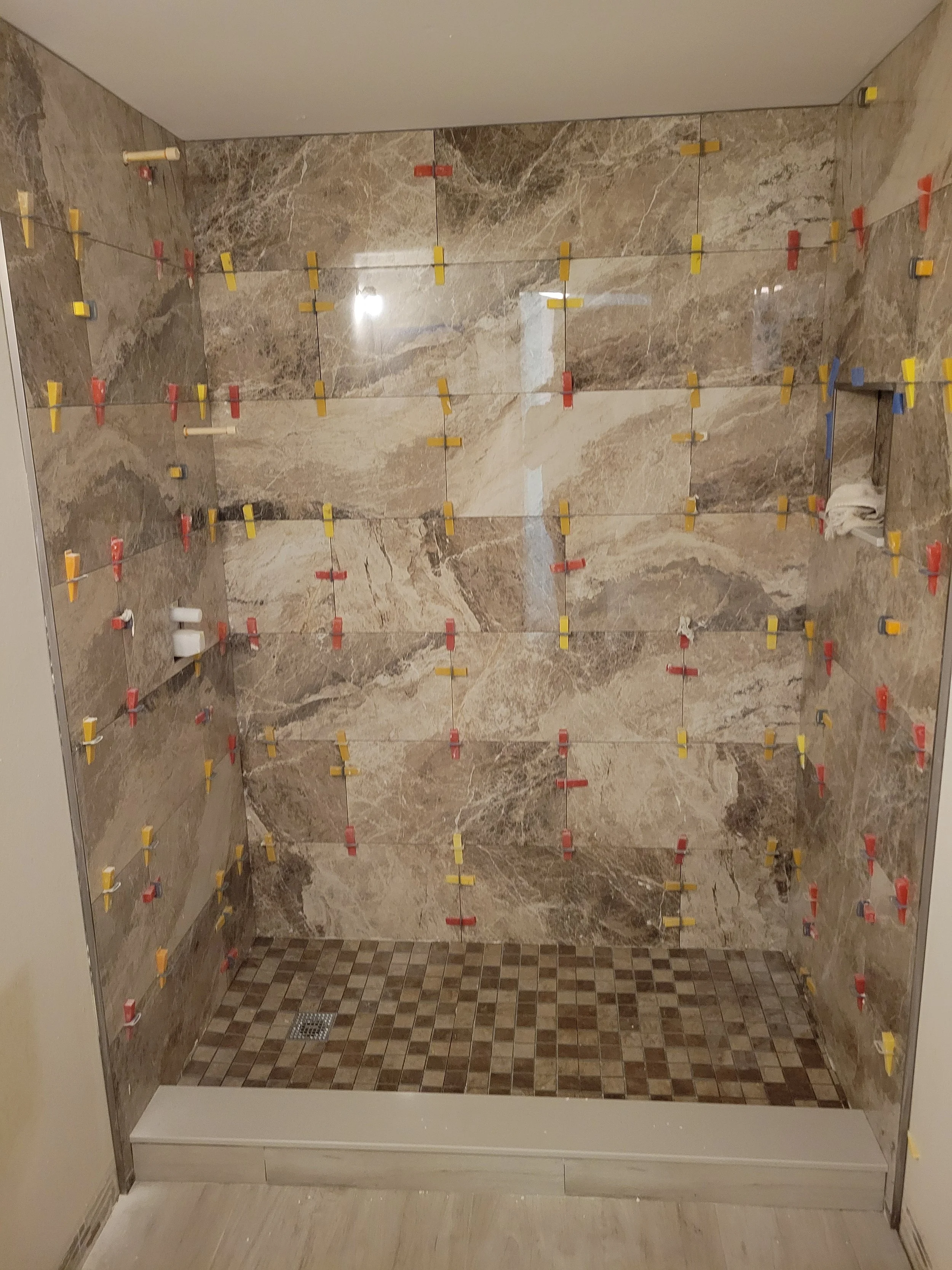 Shower stall with marble tiles and multiple color-coded tile spacers for tiling.