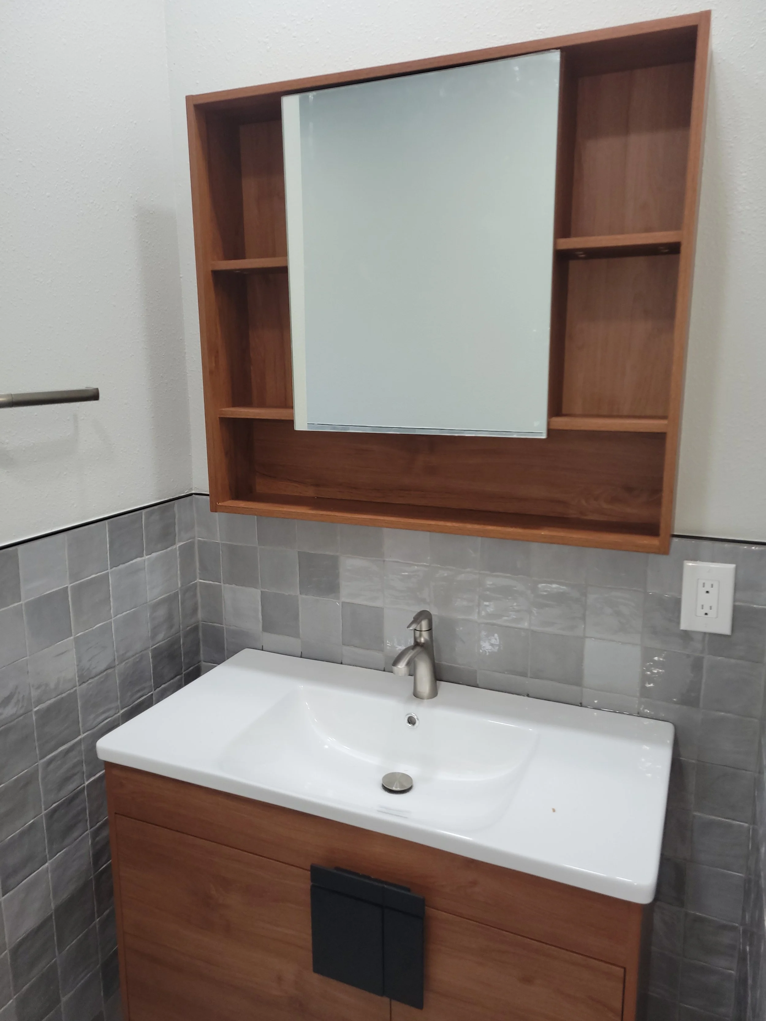 Bathroom vanity with wooden cabinet, white sink with silver faucet, gray tiled wall, and mirrored medicine cabinet