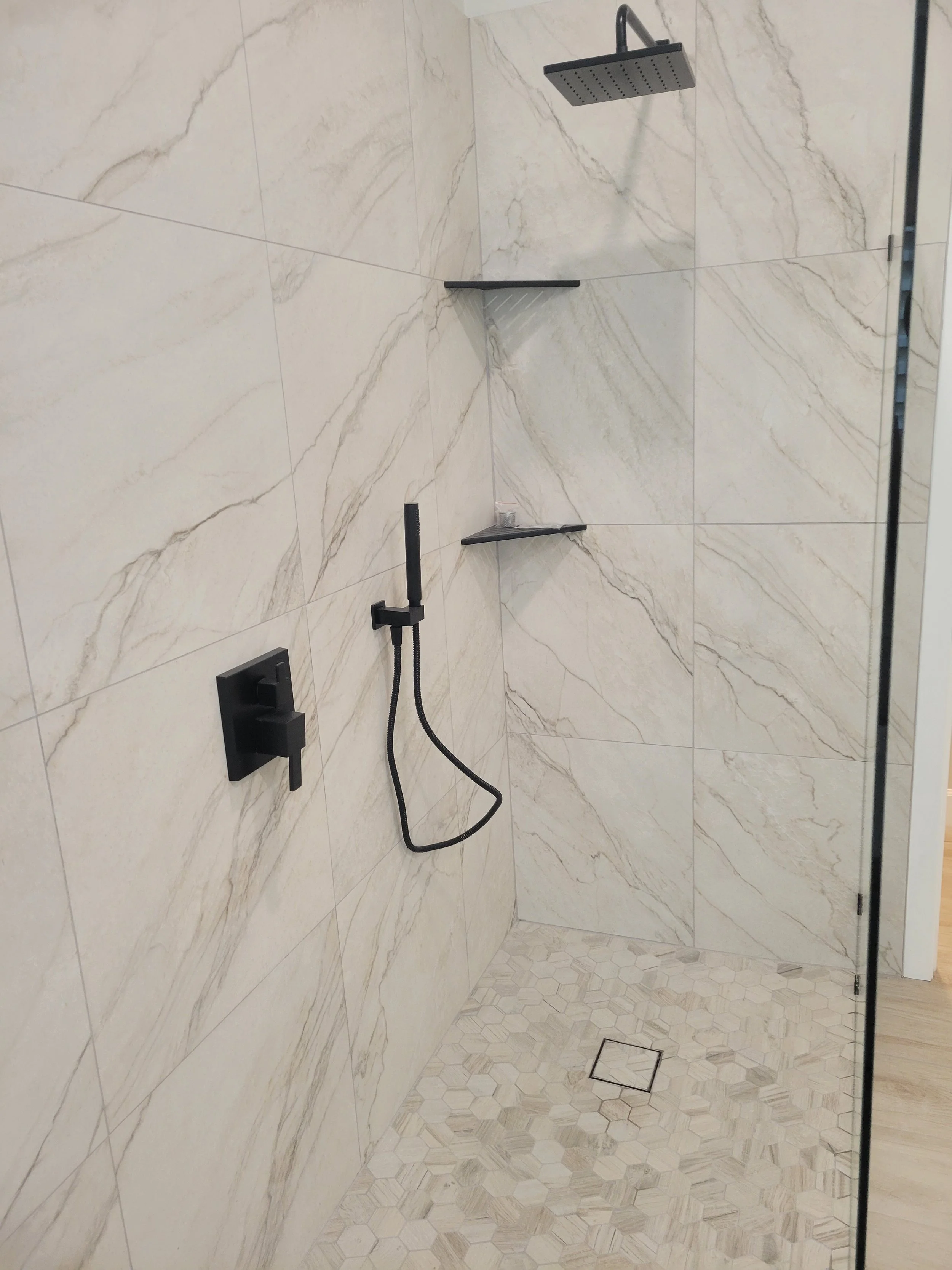 Modern walk-in shower with large beige marble-patterned tiles, black fixtures, and a rainfall showerhead.