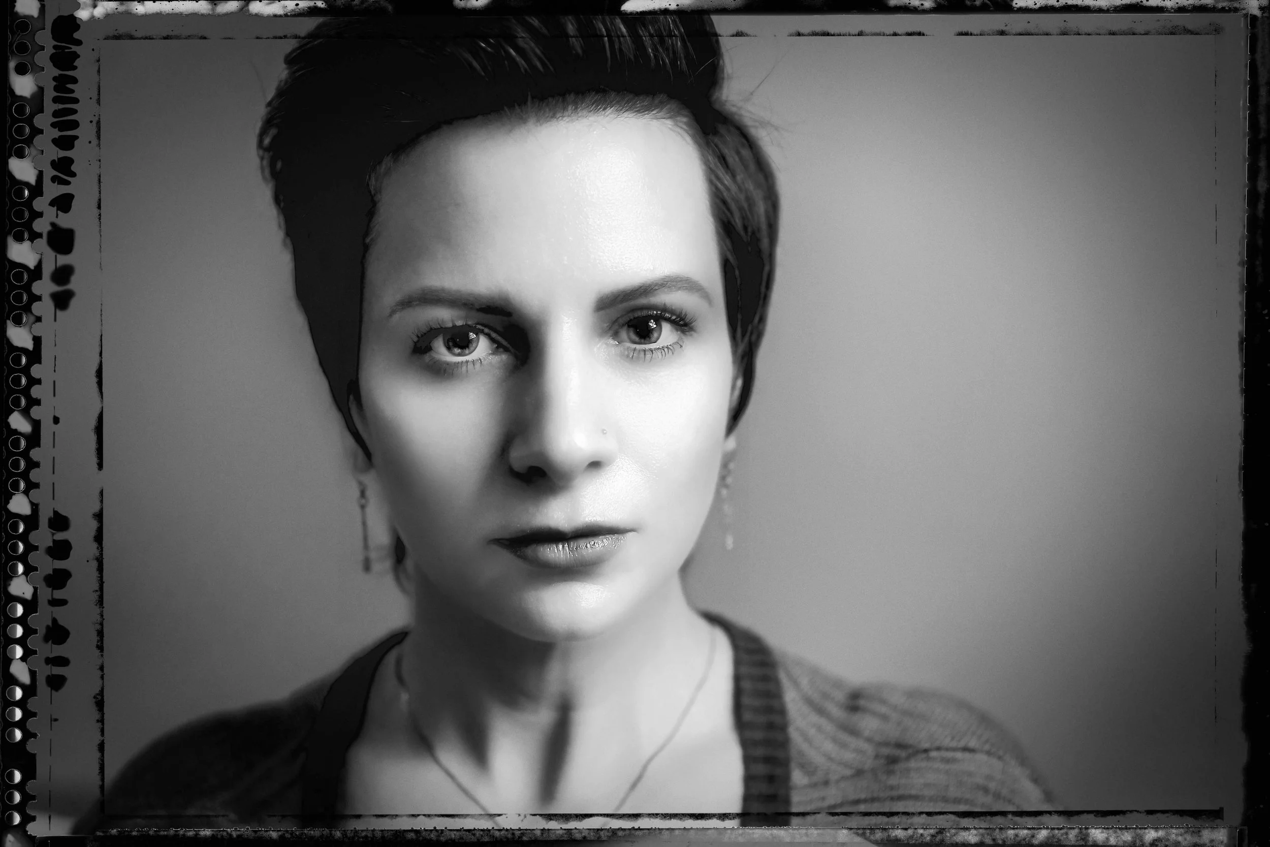 Black and white portrait of a woman with short hair, wearing earrings and a necklace, looking directly into the camera.
