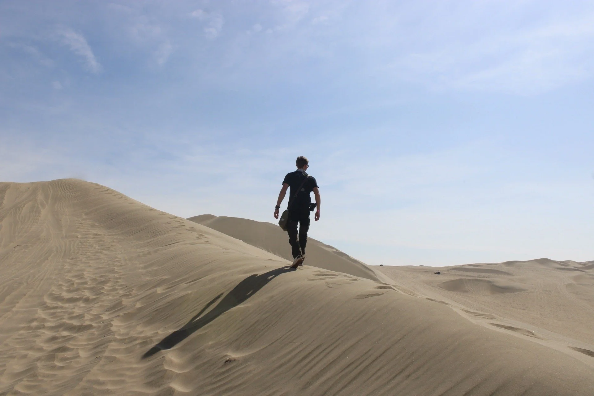 Person walking on sand dunes under a clear blue sky.