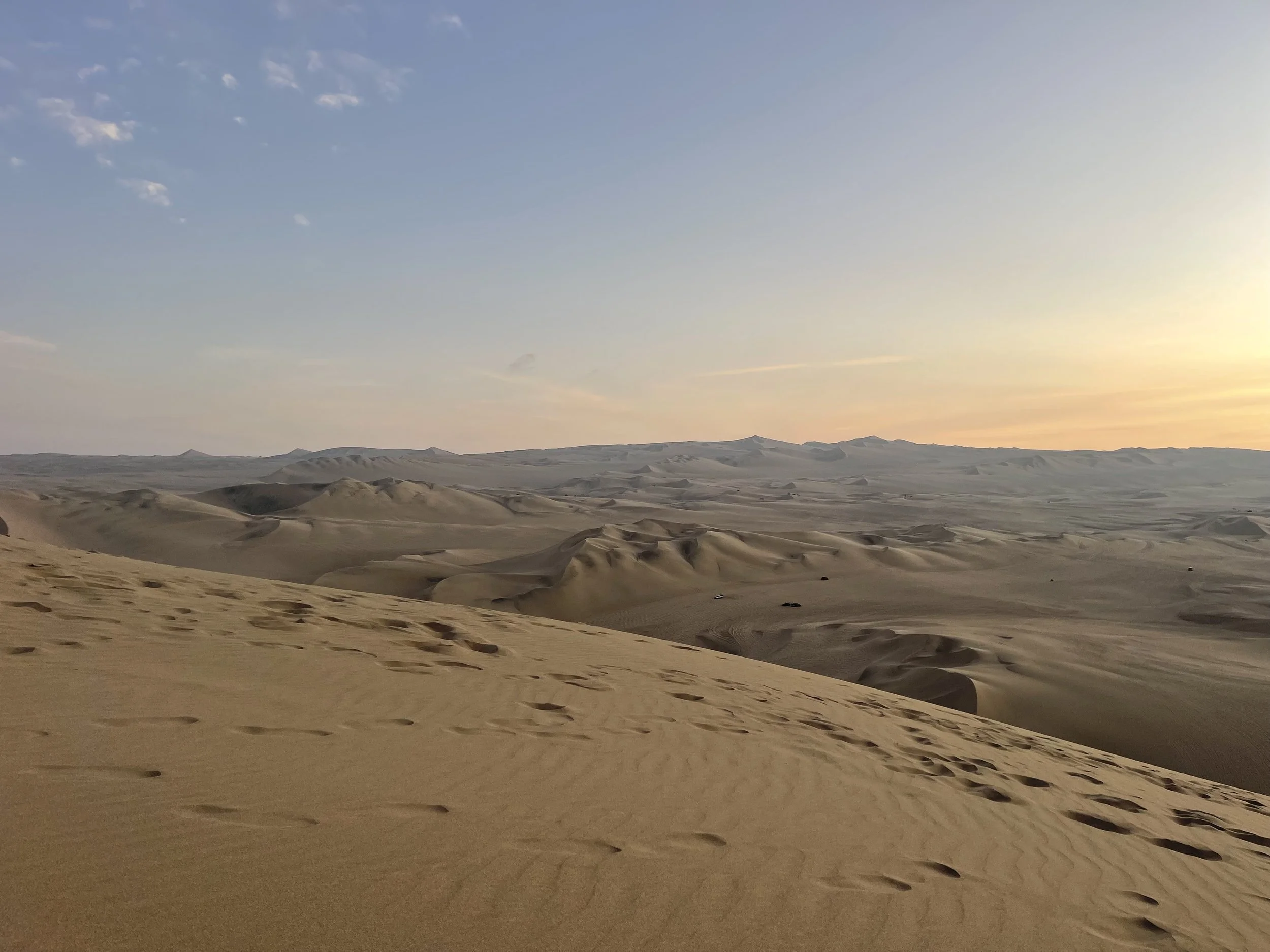 A vast desert landscape with sand dunes under a clear sky at sunset.