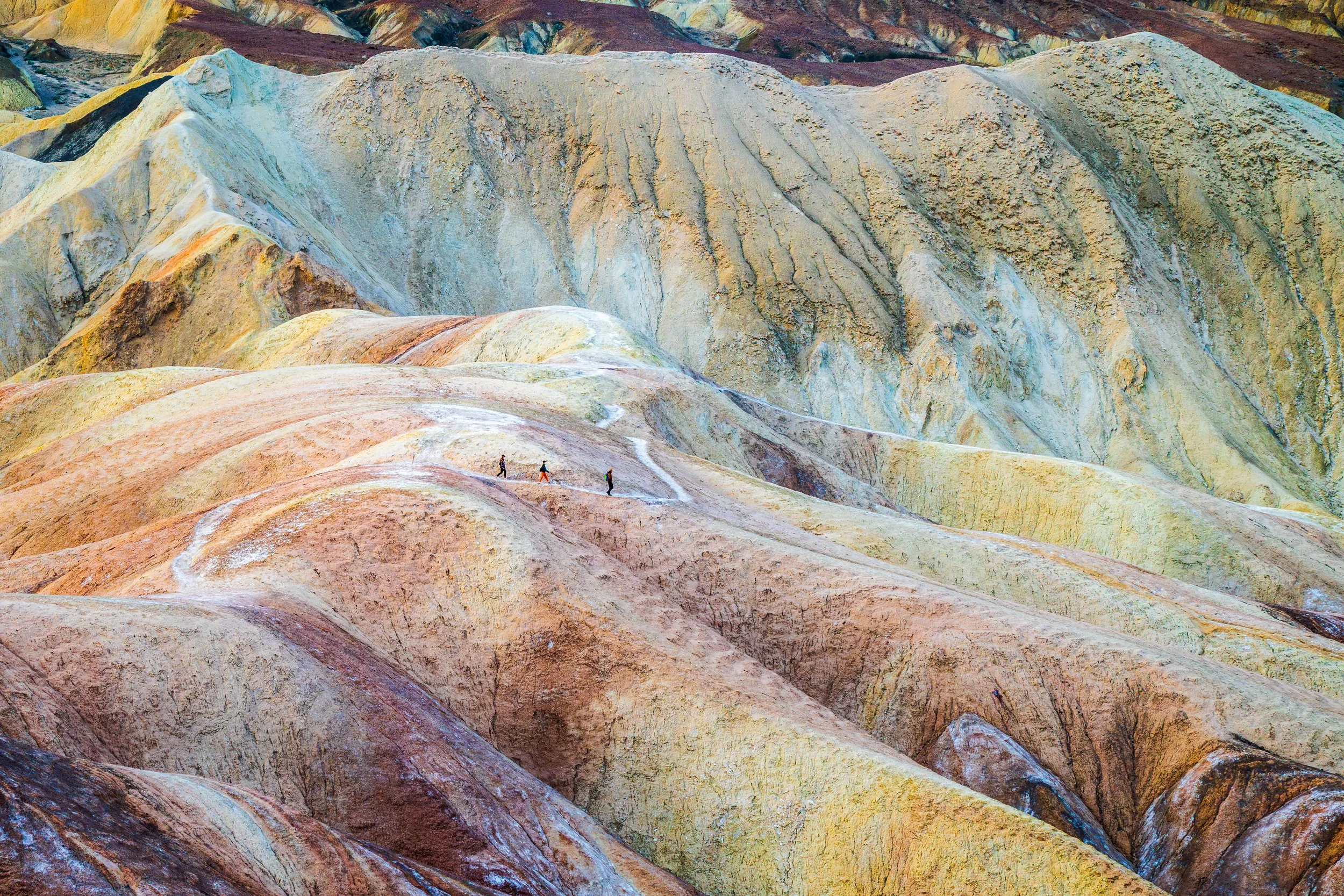 Travelers - taken just after sunrise at Zabriskie Point. Three  lone hikers trek through the fantastic rock formations.
