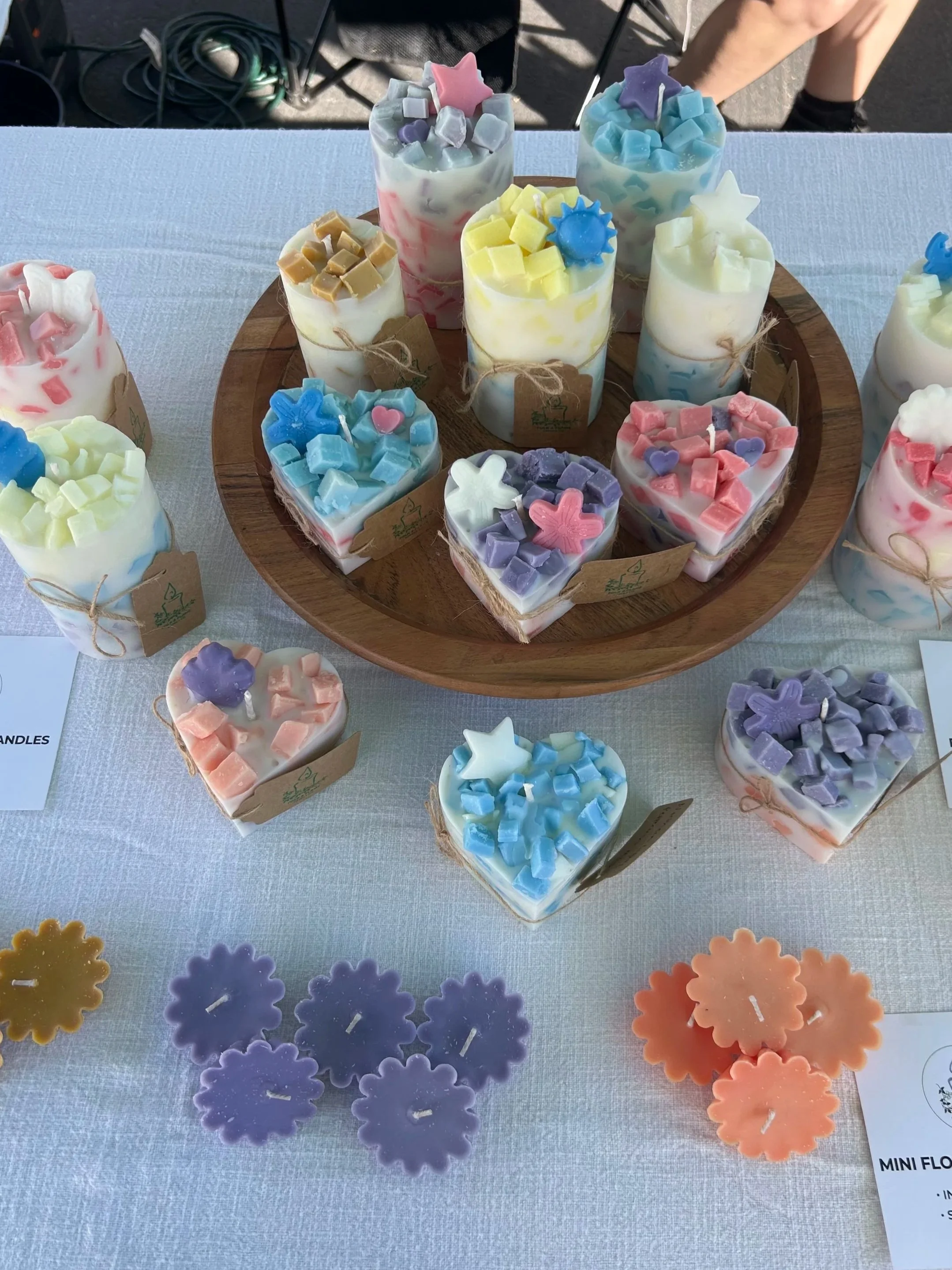 Display of colorful floating candles shaped like flowers. Another display of "mosaic" pre-made pillar candles on a Lazy Susan at a local farmer's market.