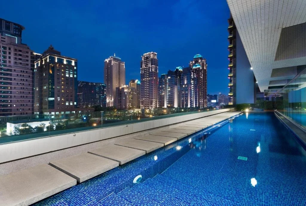Rooftop swimming pool overlooking a Taiwanese city skyline at night.