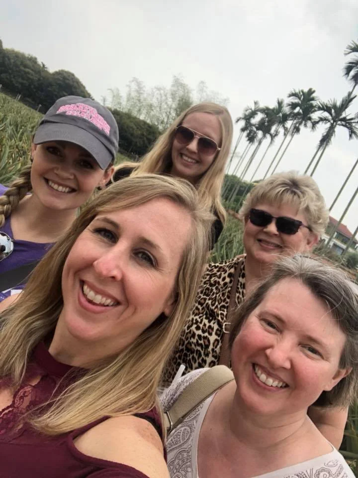A group of women stand in front of a pineapple field smiling into the camera during a Cultural Experience to Taiwan with Tricia Pomering.