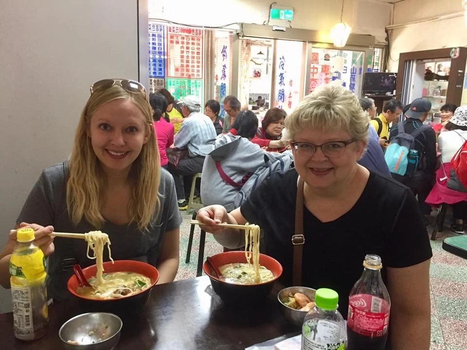 Two women enjoy bowls of noodles in a restaurant in Taiwan during a Tricia Pomering Cultural Experience.