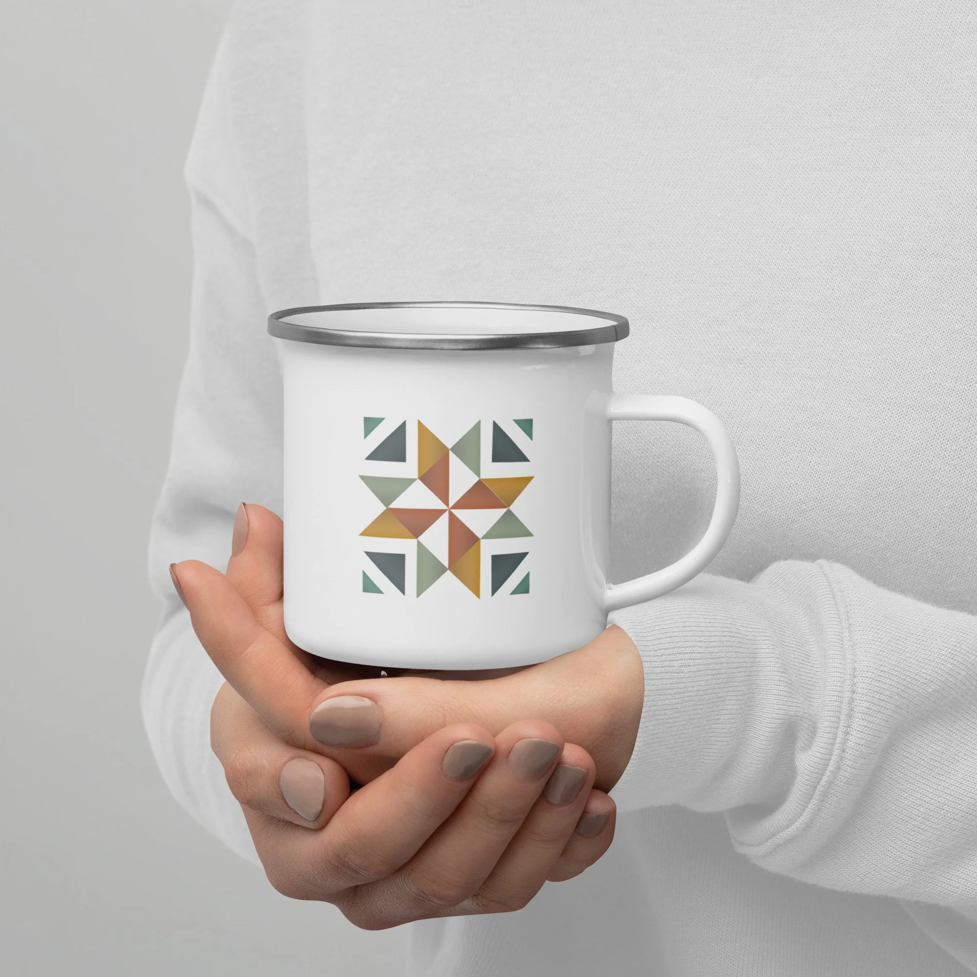 A person holding a beautiful white camping mug with a silver lip and a fun quilt block square on the front and back.