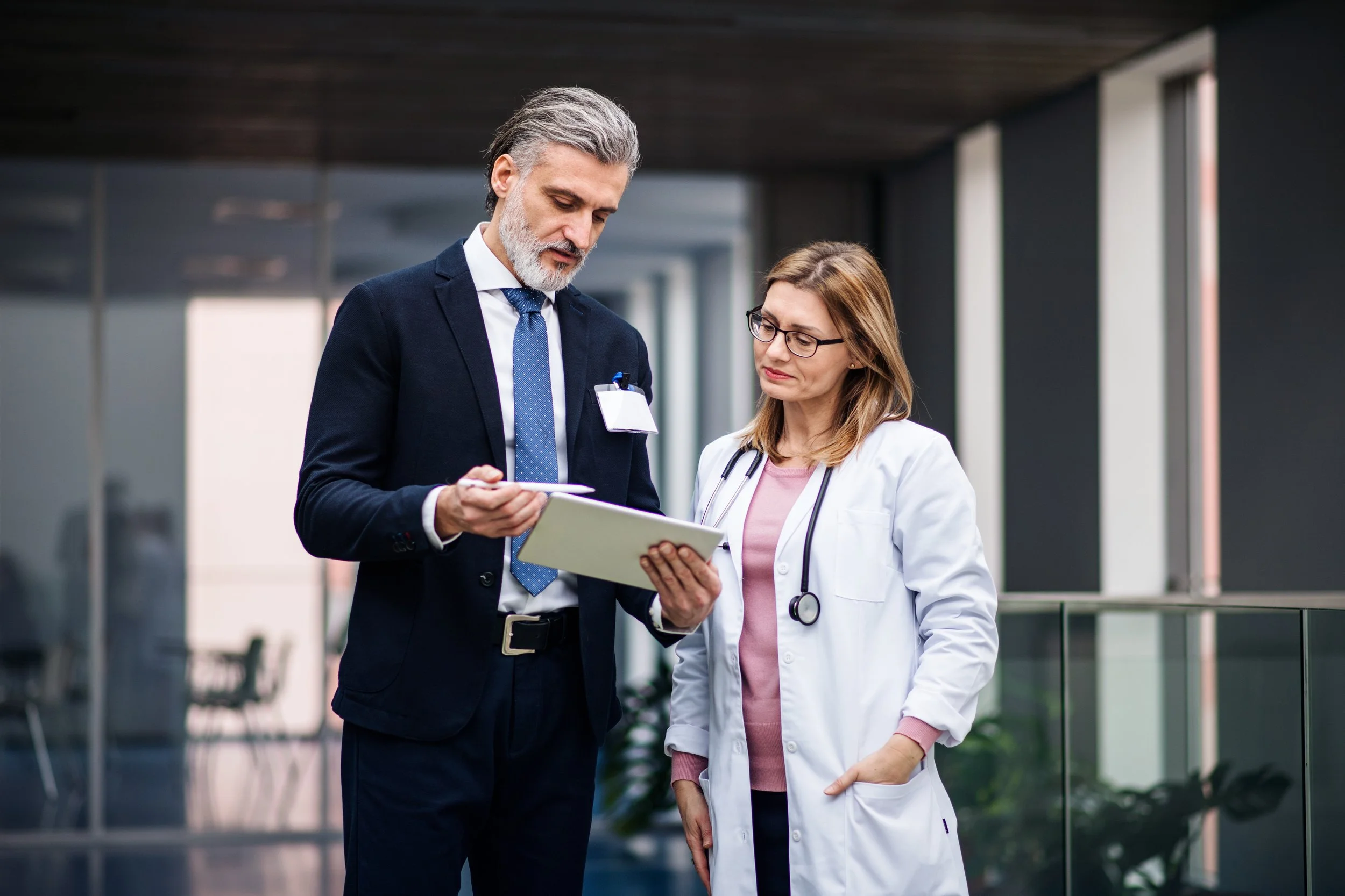 Nurse chatting with a businessman who are both looking at a tablet.