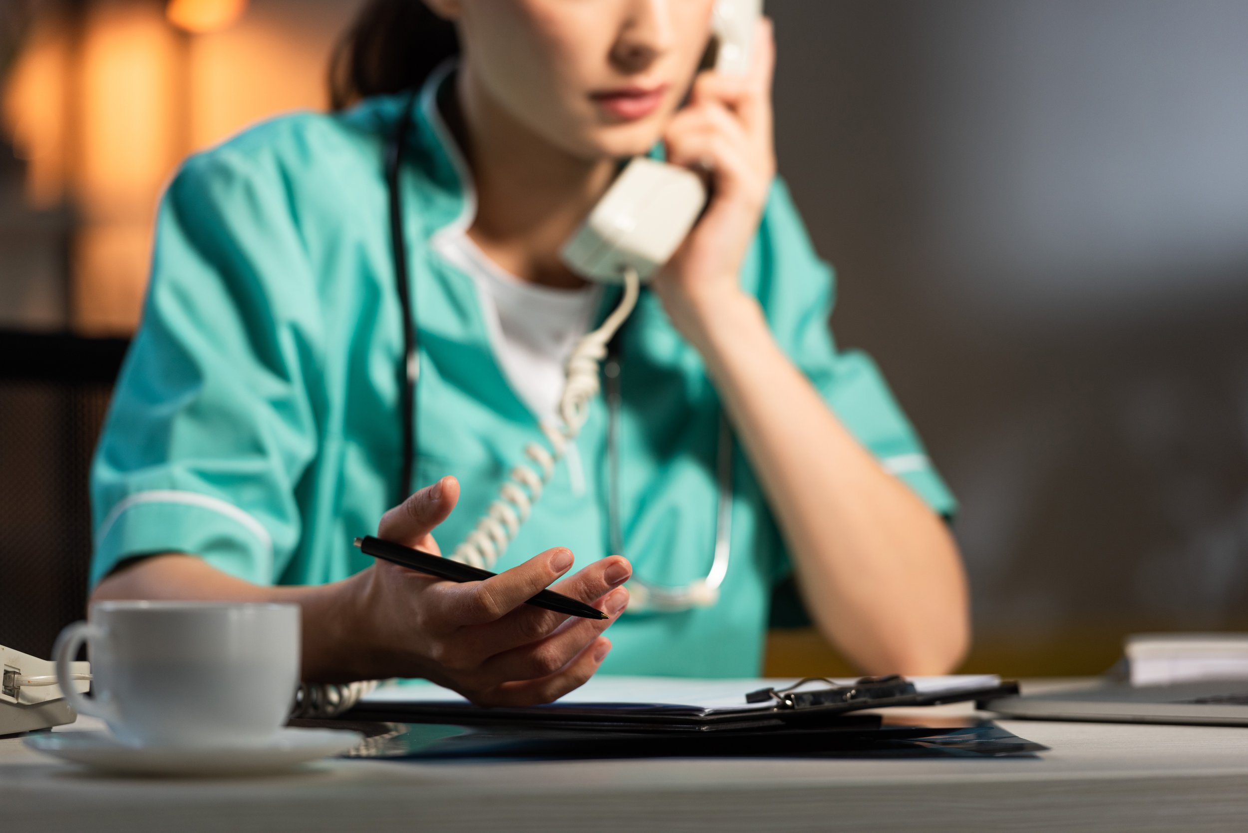 Woman nurse in scrubs on the phone holding a pen, asking a question to the person on the line.