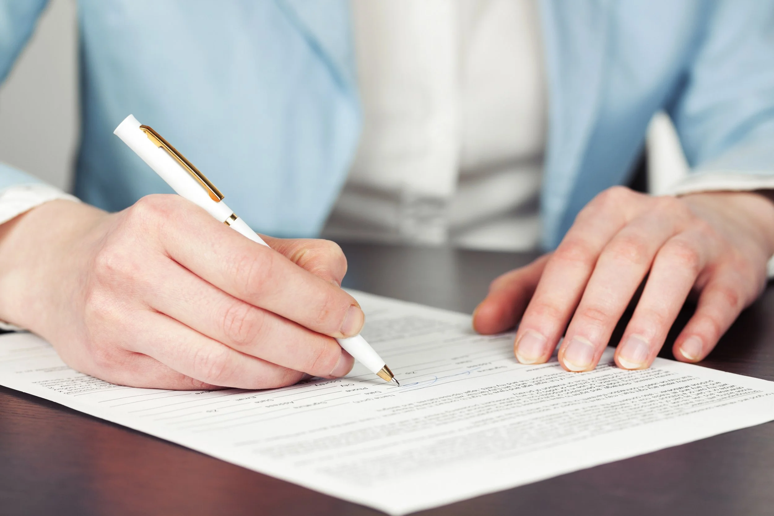 Man sitting at a desk using a pen to fill out a form.