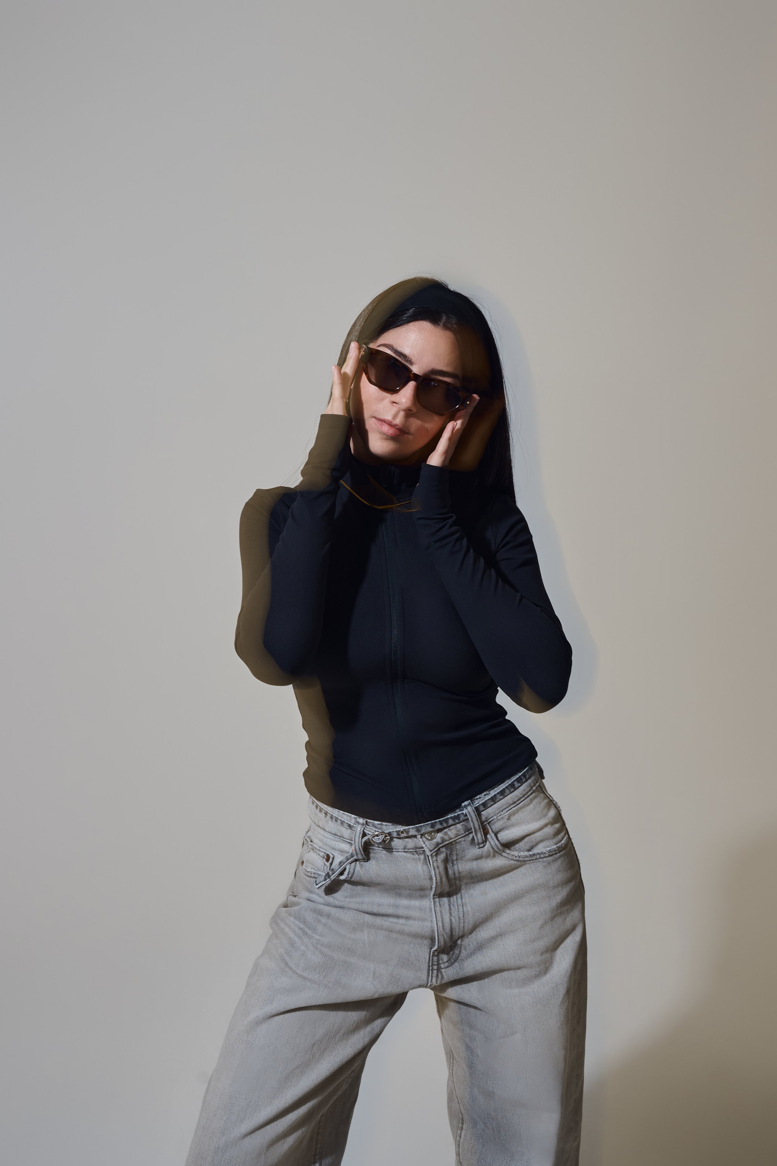 Portrait mit Doppelbelichtungseffekt. Person im schwarzen Zip-Up und hellen Jeans trägt eine braune Sonnenbrille.