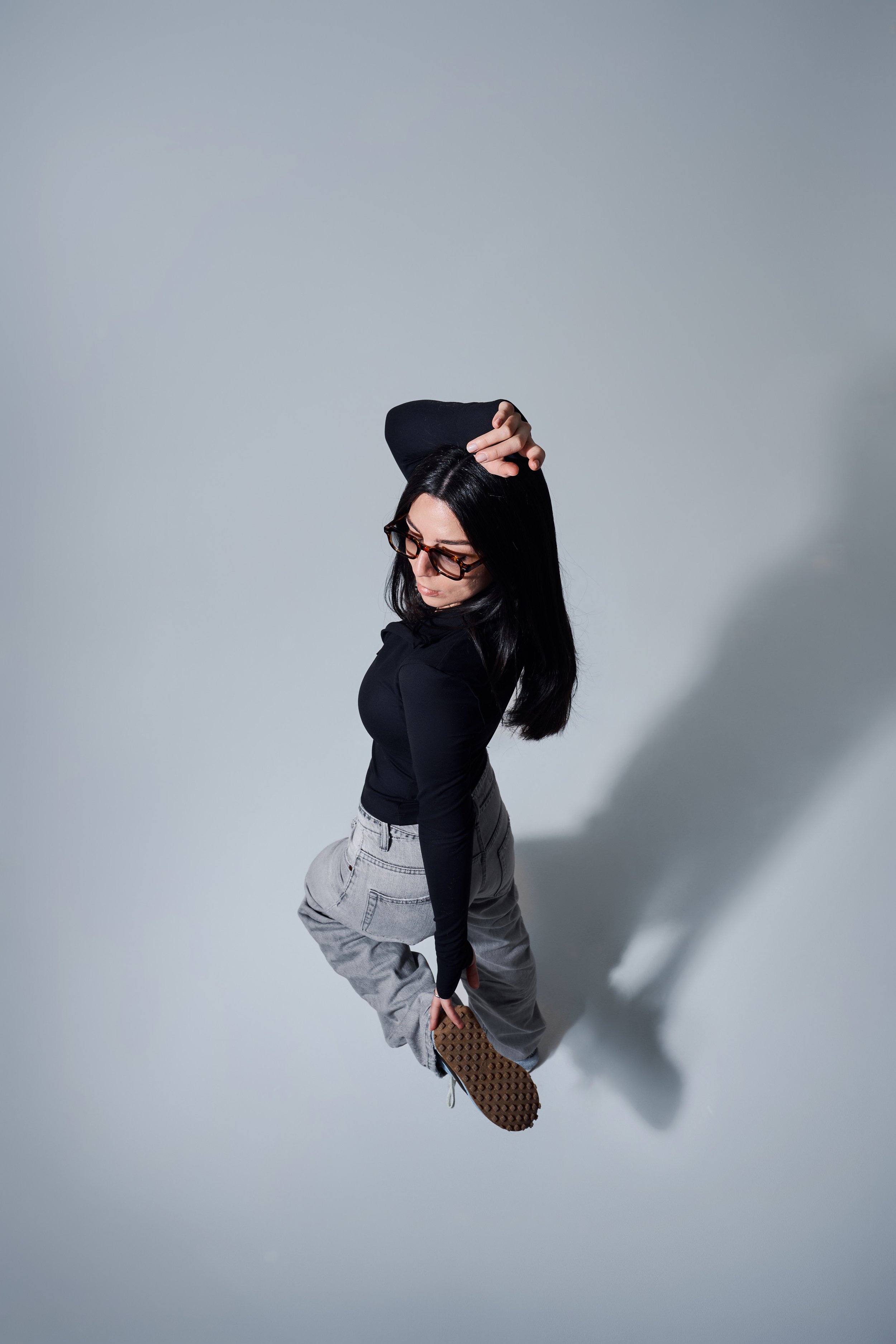 Studioaufnahme aus der Vogelperspektive. Person in Pose auf hellem Boden, schwarzes Oberteil und helle Jeans.