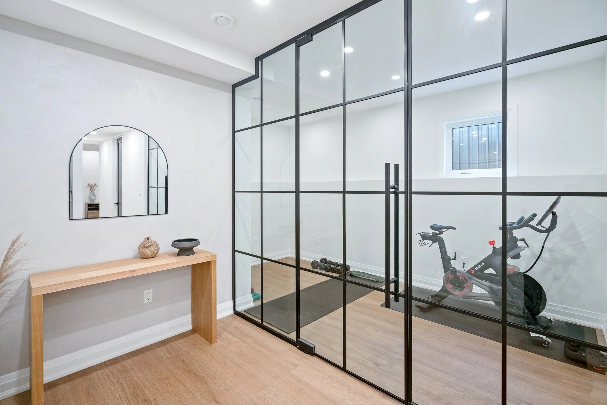 A modern home gym with a glass wall, an exercise bike, a small window, and minimal decor.