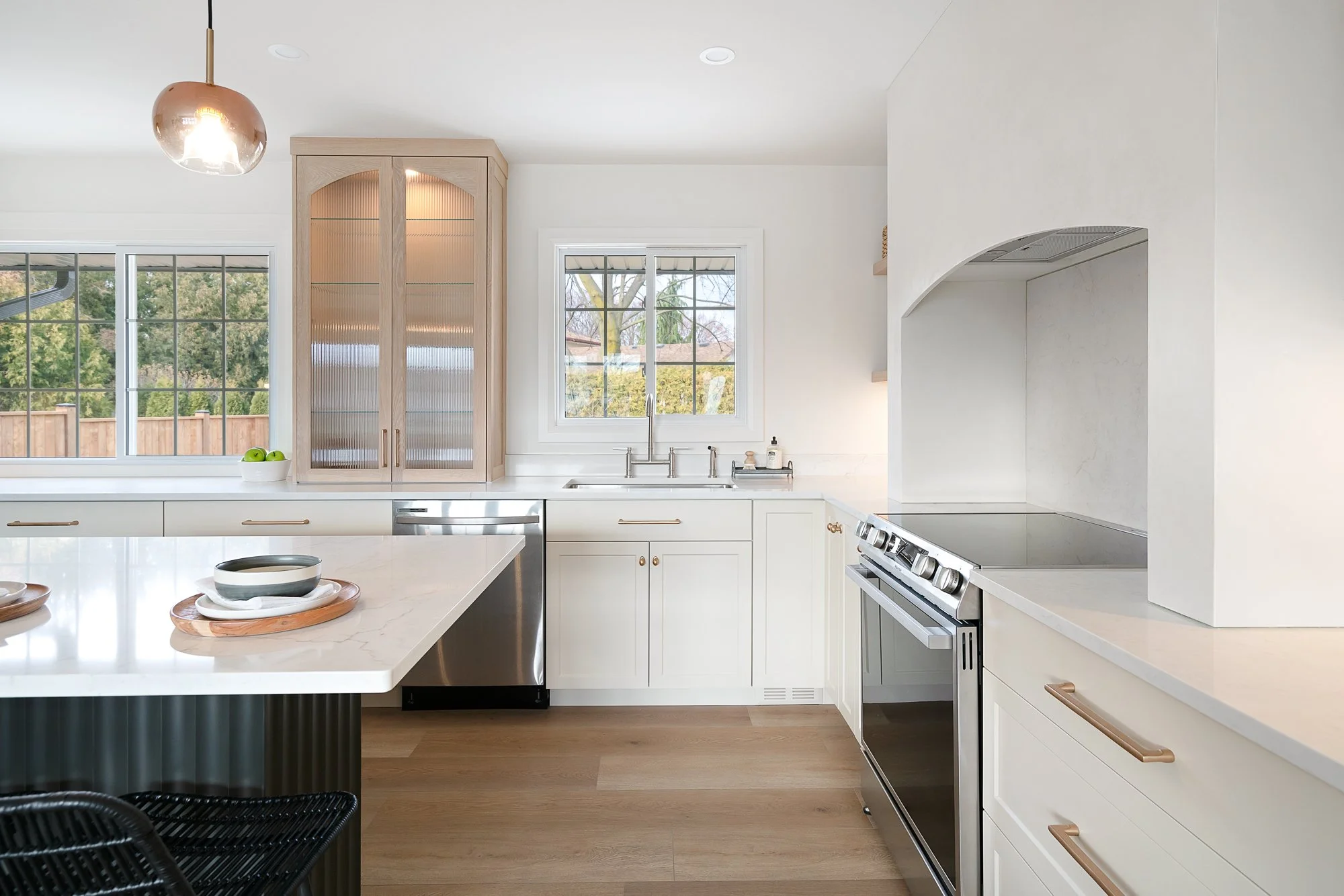 Modern kitchen with white cabinets, stainless steel appliances, a marble countertop island, large windows, and wooden flooring.