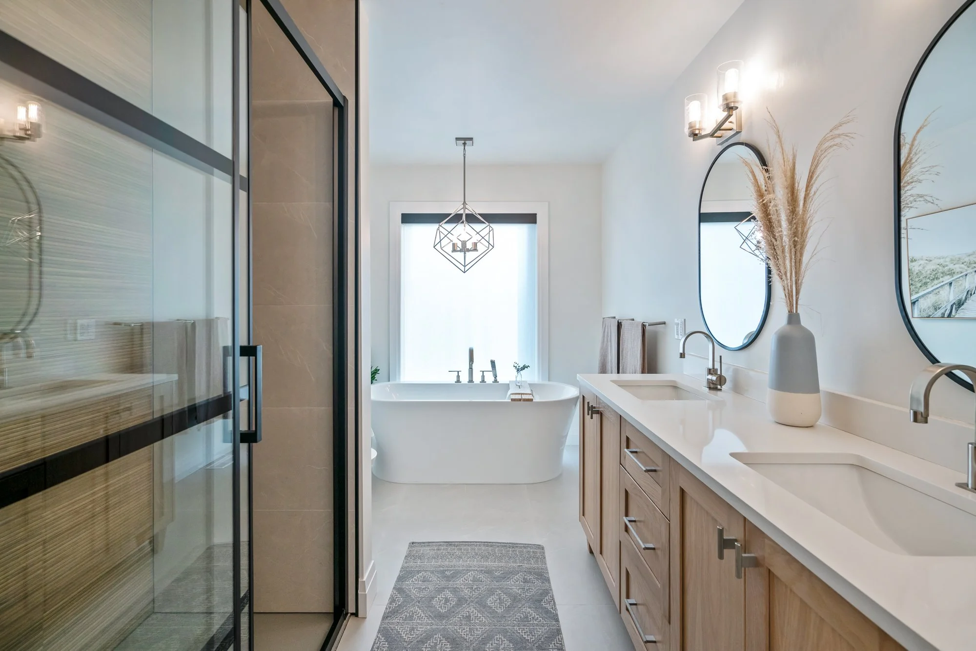 Modern bathroom with dual sinks, a freestanding bathtub, and a glass shower enclosure, decorated with neutral tones and minimal decor.