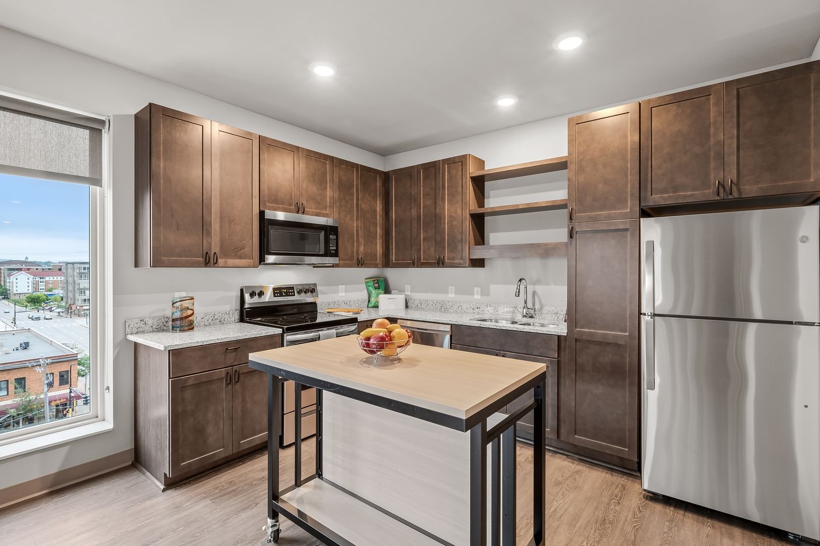Modern kitchen with wooden cabinets, stainless steel appliances, a small kitchen island, and a window showing a city view.