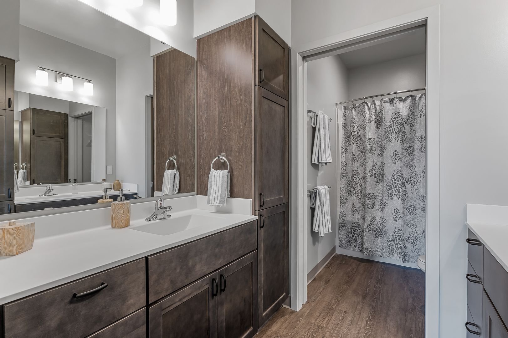 Bathroom with vanity, large mirror, wood cabinets, towel rings with towels, and a shower area with animal print curtain.