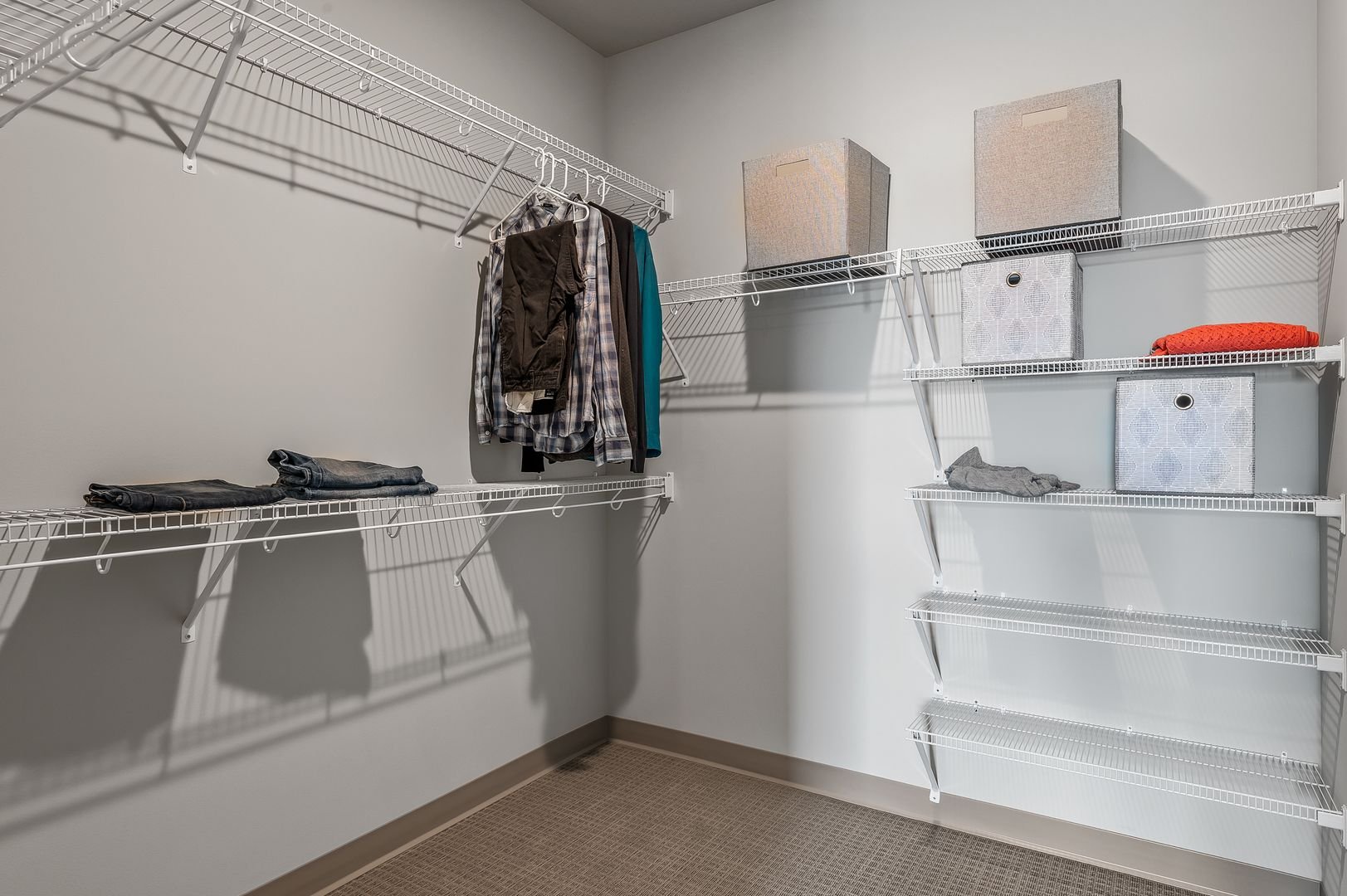 Walk-in closet with white wire shelves, some clothing on the left shelf, and storage boxes on the right shelves.