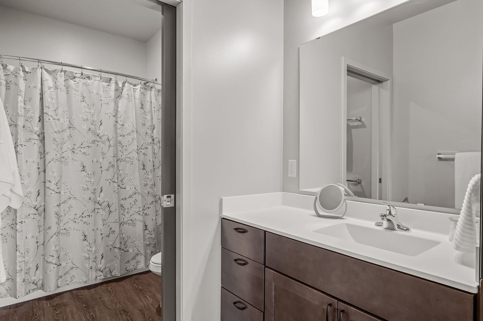 Bathroom with a vanity mirror, sink, and wooden cabinet; shower with floral curtain.
