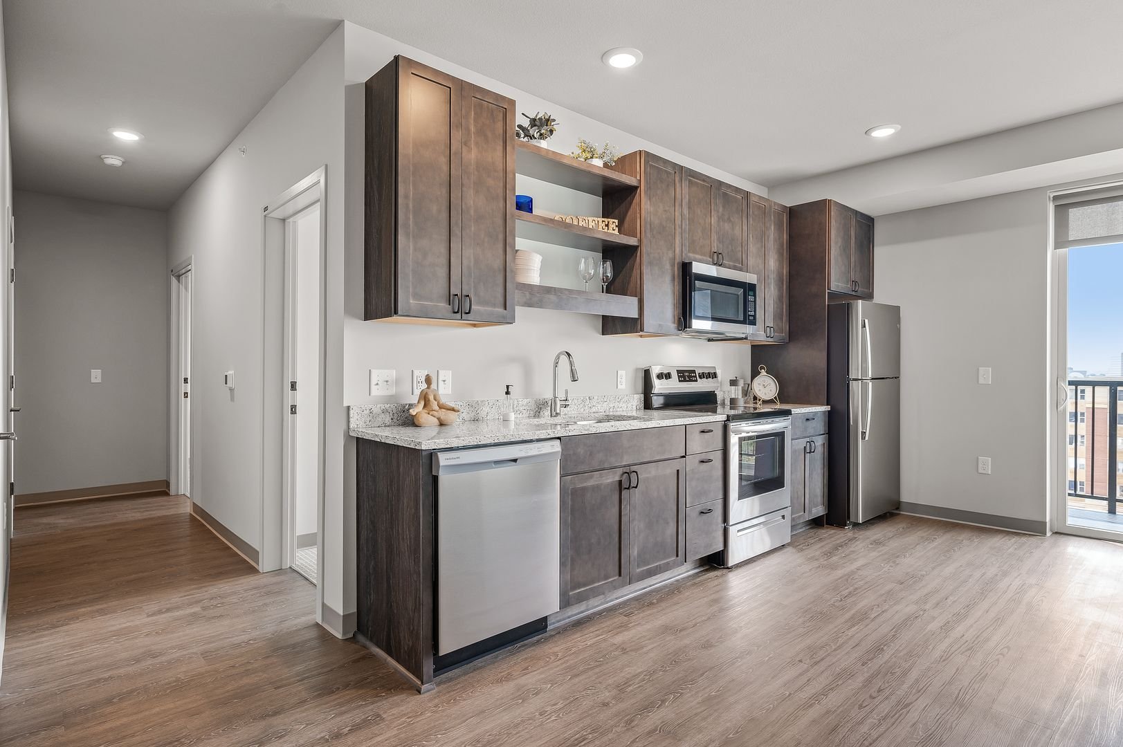 Modern kitchen with wooden cabinets, stainless steel appliances, granite countertops, and a sliding glass door leading to a balcony with a city view.