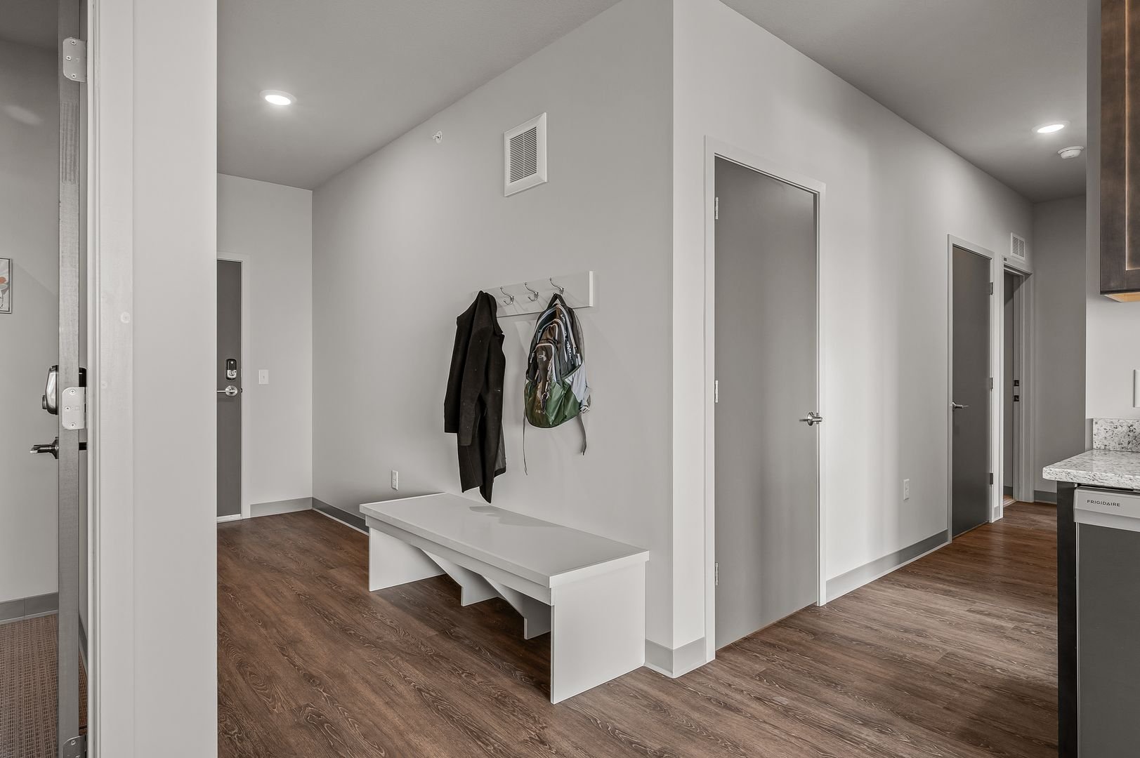 Entryway with white bench, wall hooks with jackets and backpack, painted walls, and hardwood floor.