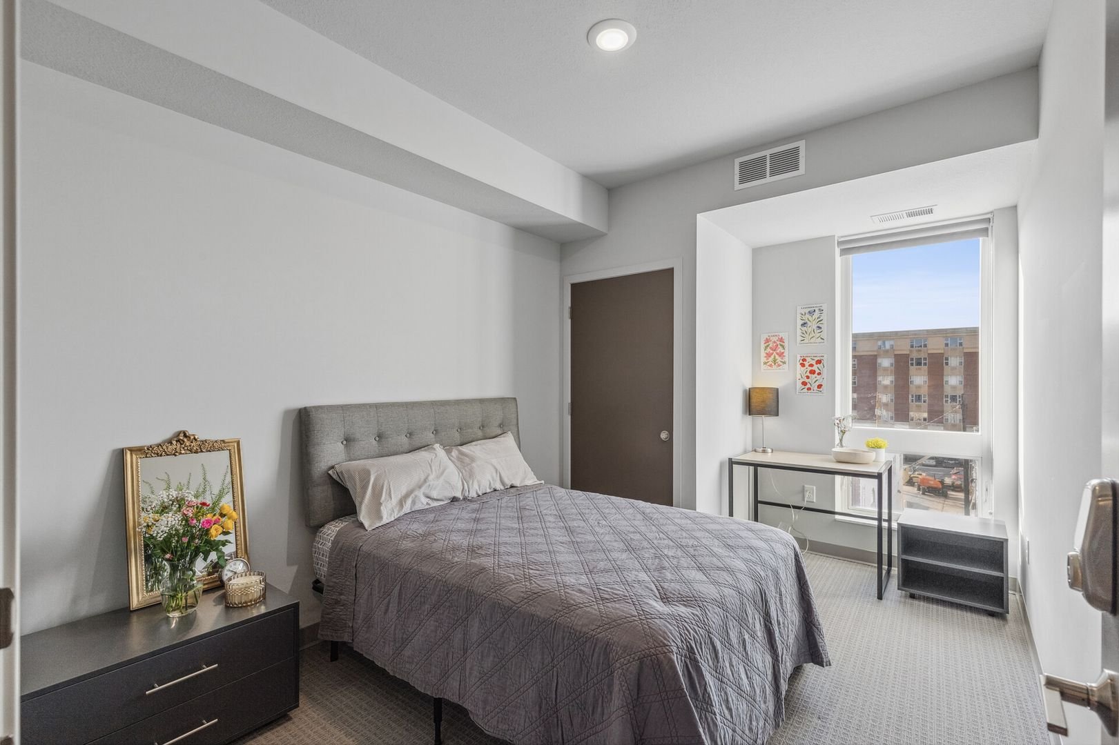 A furnished bedroom with a bed featuring a gray headboard, white pillows, and a gray quilt.