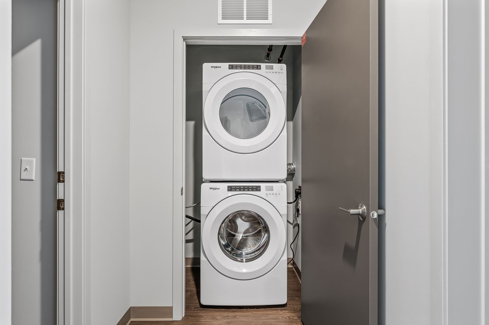 Stacked washer and dryer in a laundry closet with gray door open