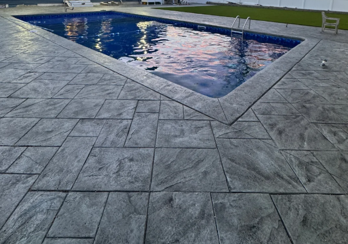 Empty backyard swimming pool with concrete deck and a grassy area in the background.