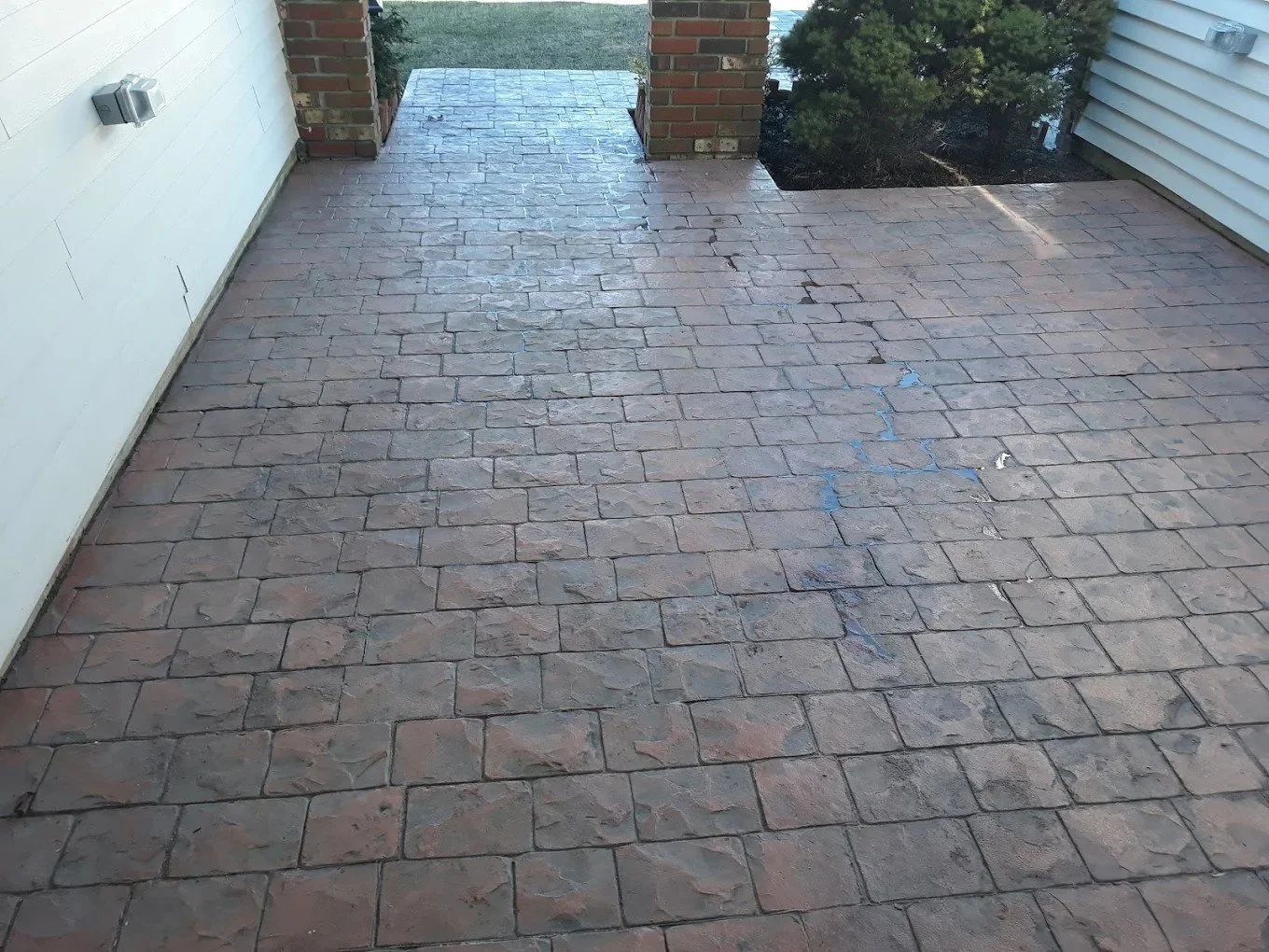 A brick patio or walkway outside a house, with some patches of blue sealant or paint and visible cracks.