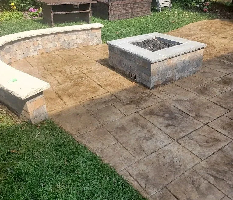 Backyard patio with stamped concrete, a fire pit, a curved brick wall, and a grassy lawn area.