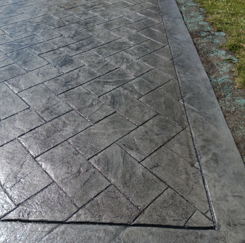 Close-up of wet, patterned concrete sidewalk with a geometric border, next to a grass edge.
