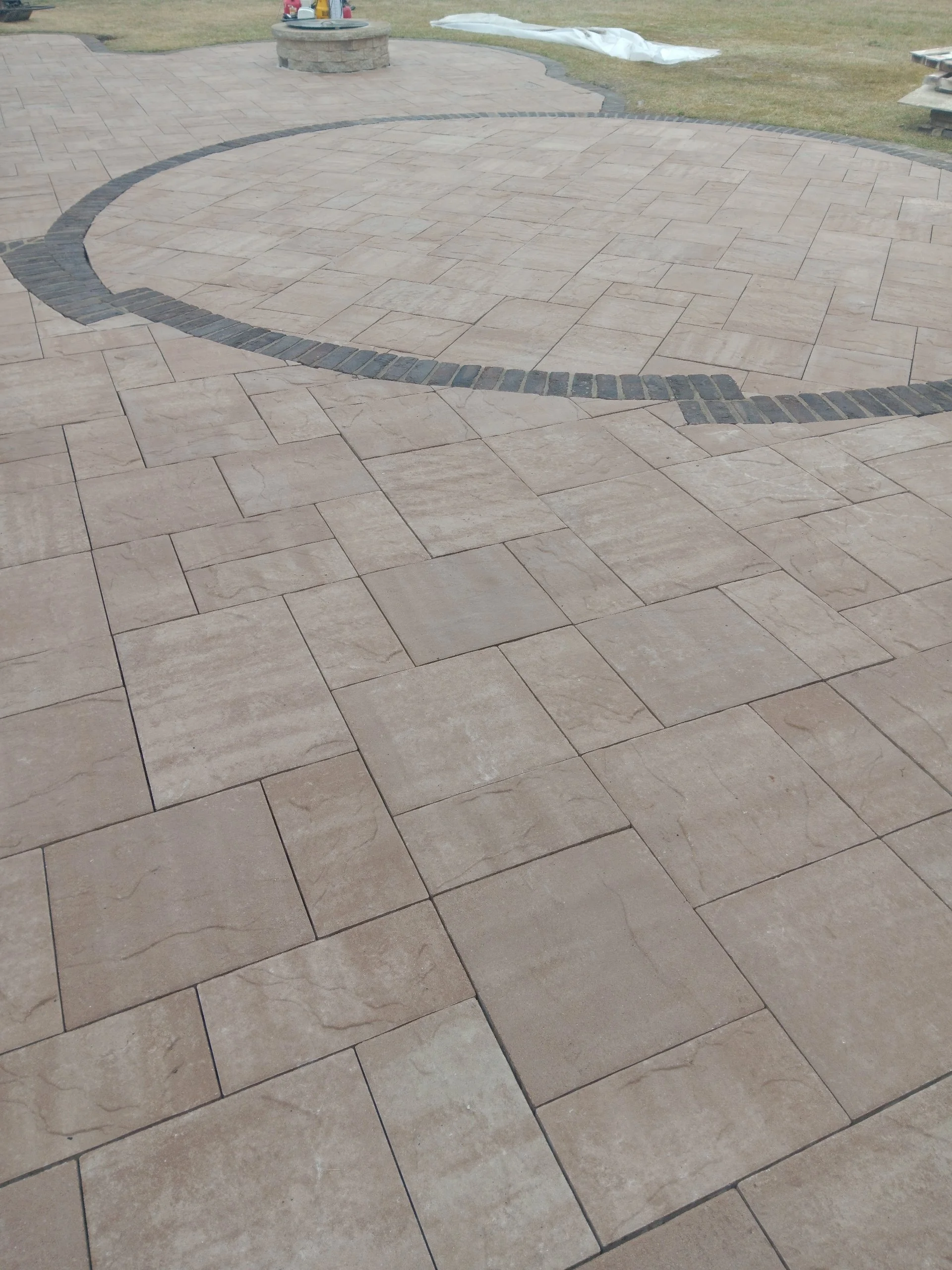 Newly laid stone patio with a curved design, featuring beige rectangular tiles with a black border in a semi-circular pattern.