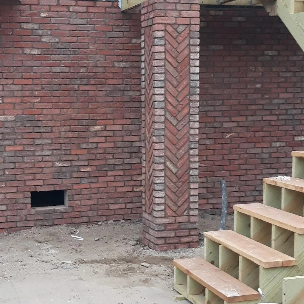 Close-up of a brick wall with a decorative brick column and unfinished wooden stairs nearby.