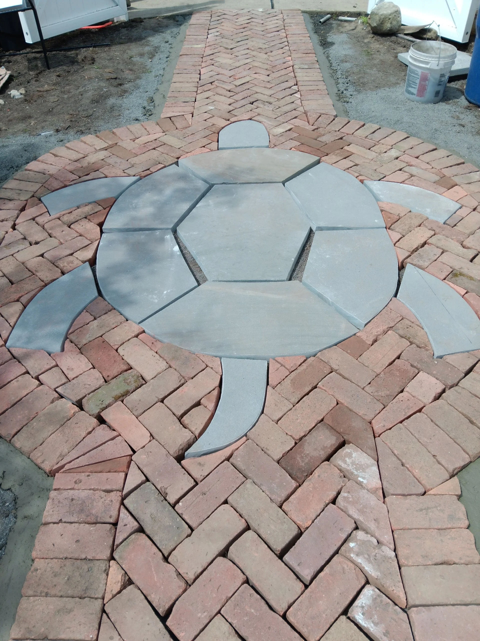 Patio with a turtle-shaped design, featuring brick paving and concrete or stone turtle elements in the center.