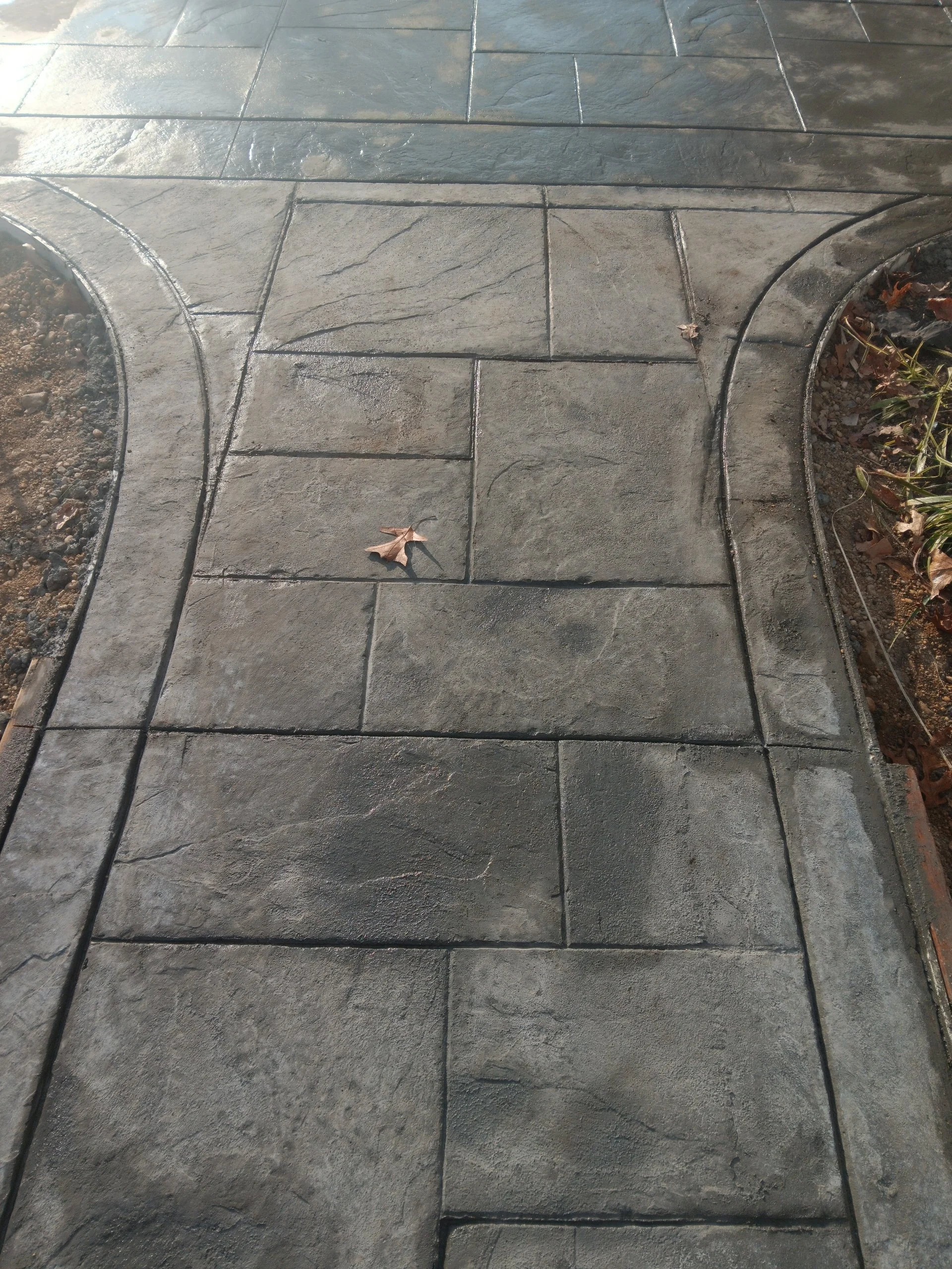 Concrete sidewalk with curved borders, one leaf on the surface, and some drag marks.