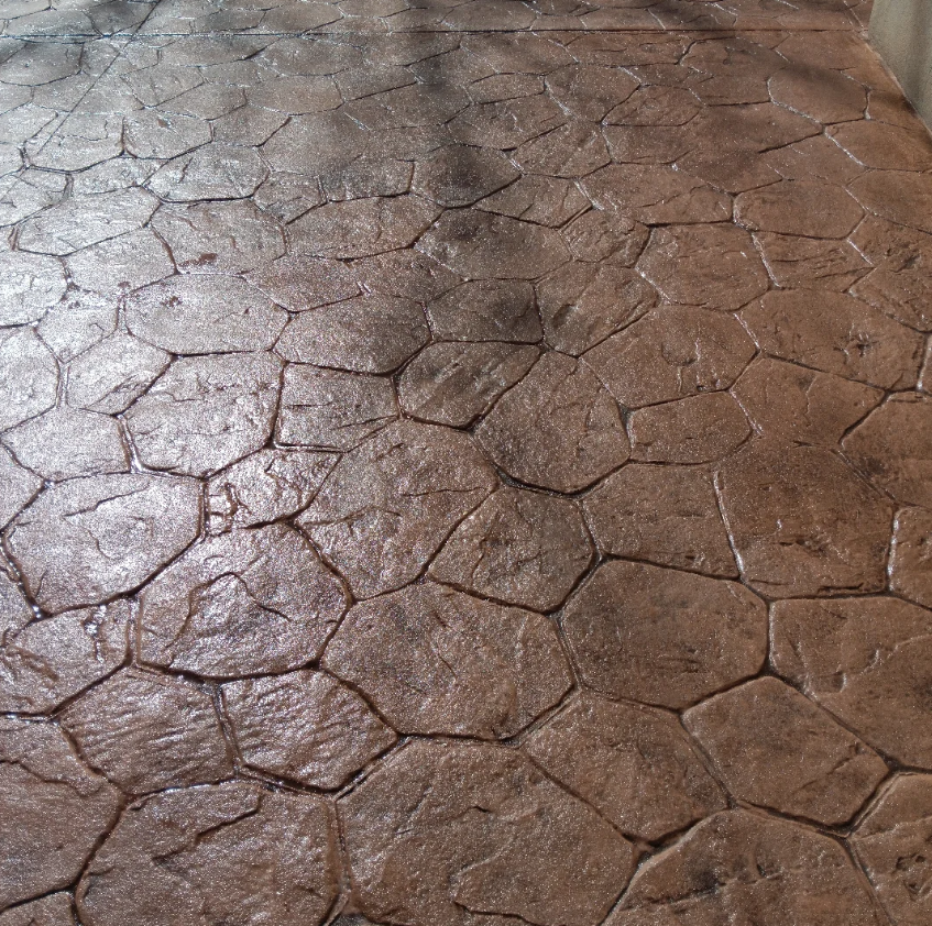 Close-up of a stamped concrete floor designed to look like irregular stones with a brown, wet finish.