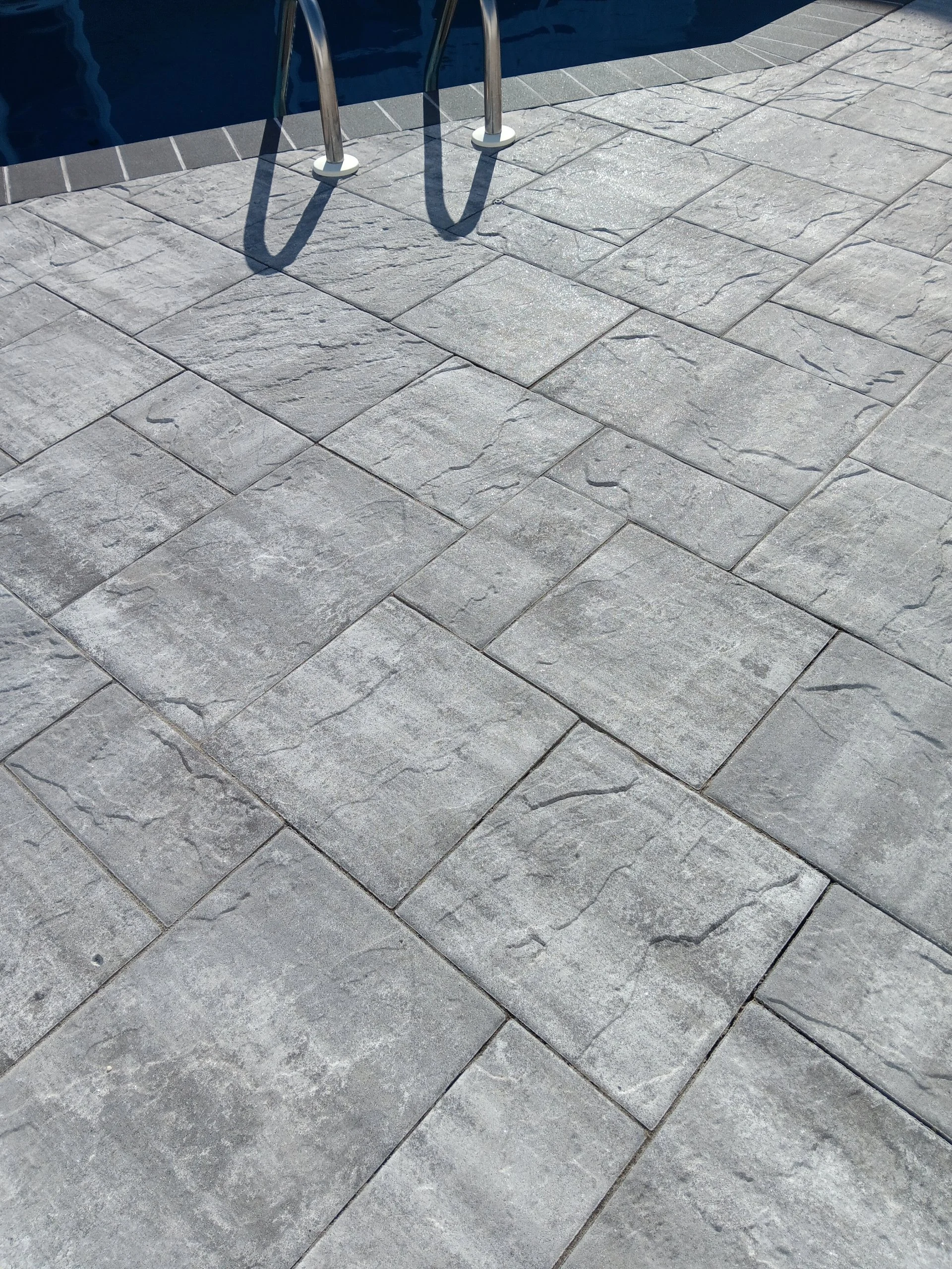 Gray stone pool deck with metal ladder leading into a blue swimming pool.