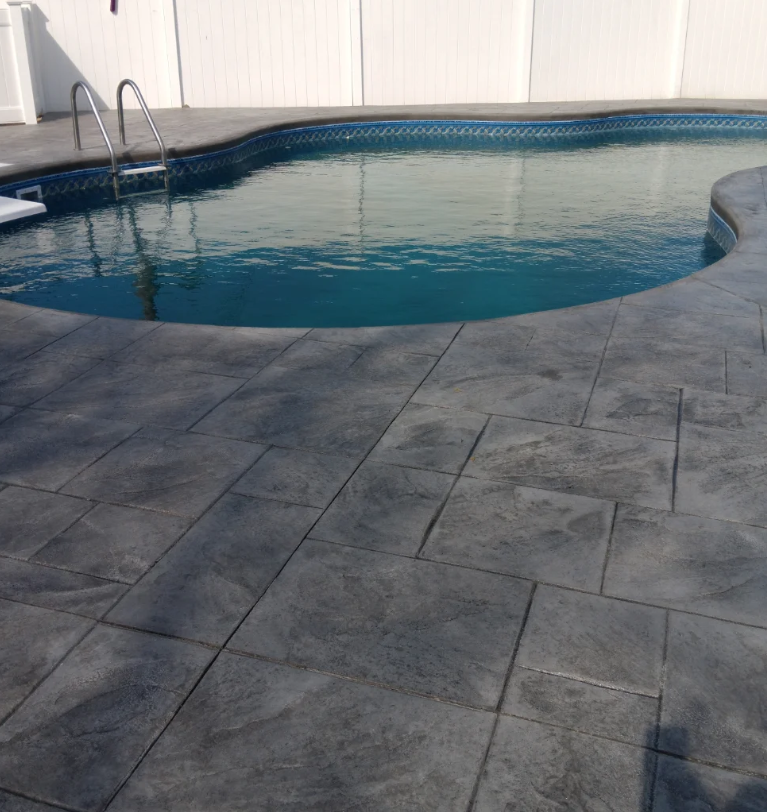 An outdoor swimming pool with a ladder and a privacy fence in the background, surrounded by a concrete deck.