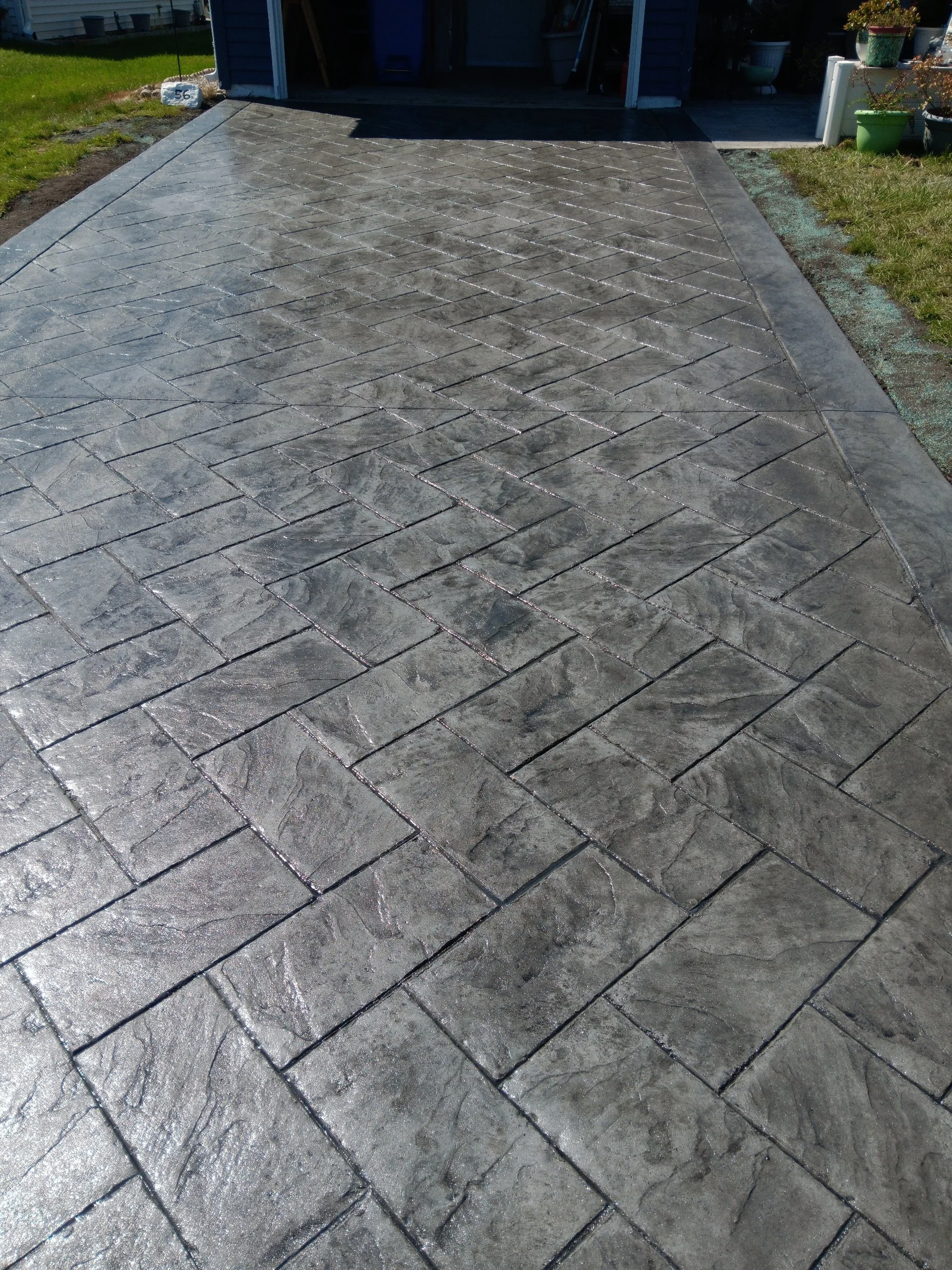 A newly paved concrete driveway with a herringbone pattern, leading to a garage, in a backyard with grass on either side.