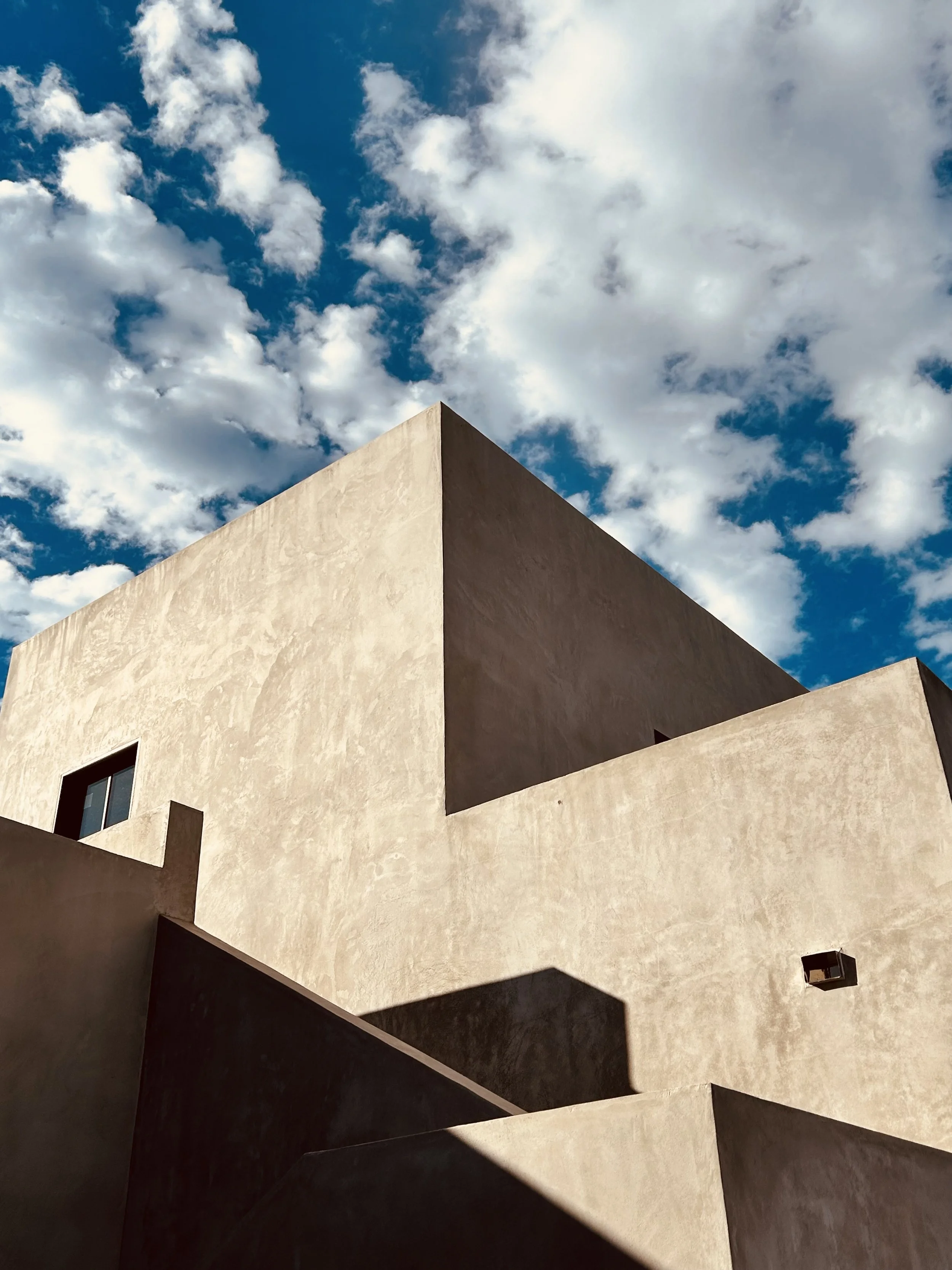 Modern architectural building with geometric shapes under a blue sky with scattered clouds.