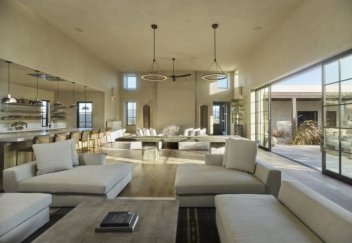 Modern open-concept living and dining area with gray sofas, bar seating, pendant lights, and large windows.